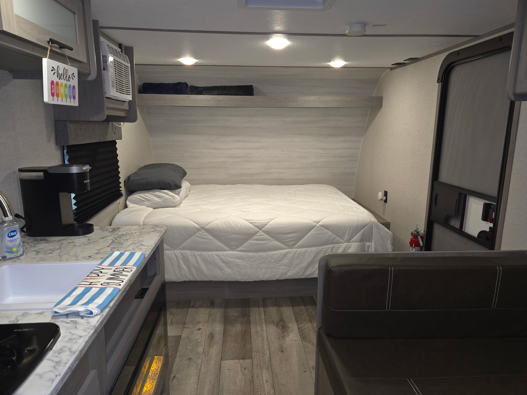 Cozy RV rental interior featuring a comfortable bed with white bedding, a compact kitchen with a sink, and a seating area.. Keystone RV CM17R23 2023
