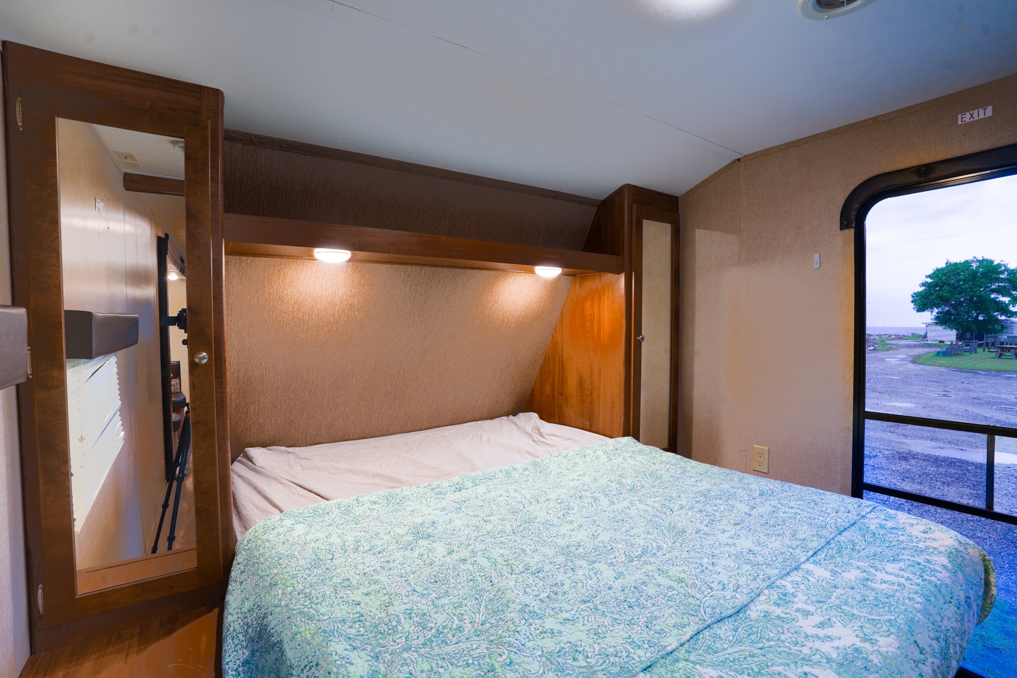 Inside this cozy RV rental: a bedroom with a blue patterned bedspread, reading lights, mirrored wardrobe, and an outdoor view.. Aspen Trail Aspen Trail Trailer 2017