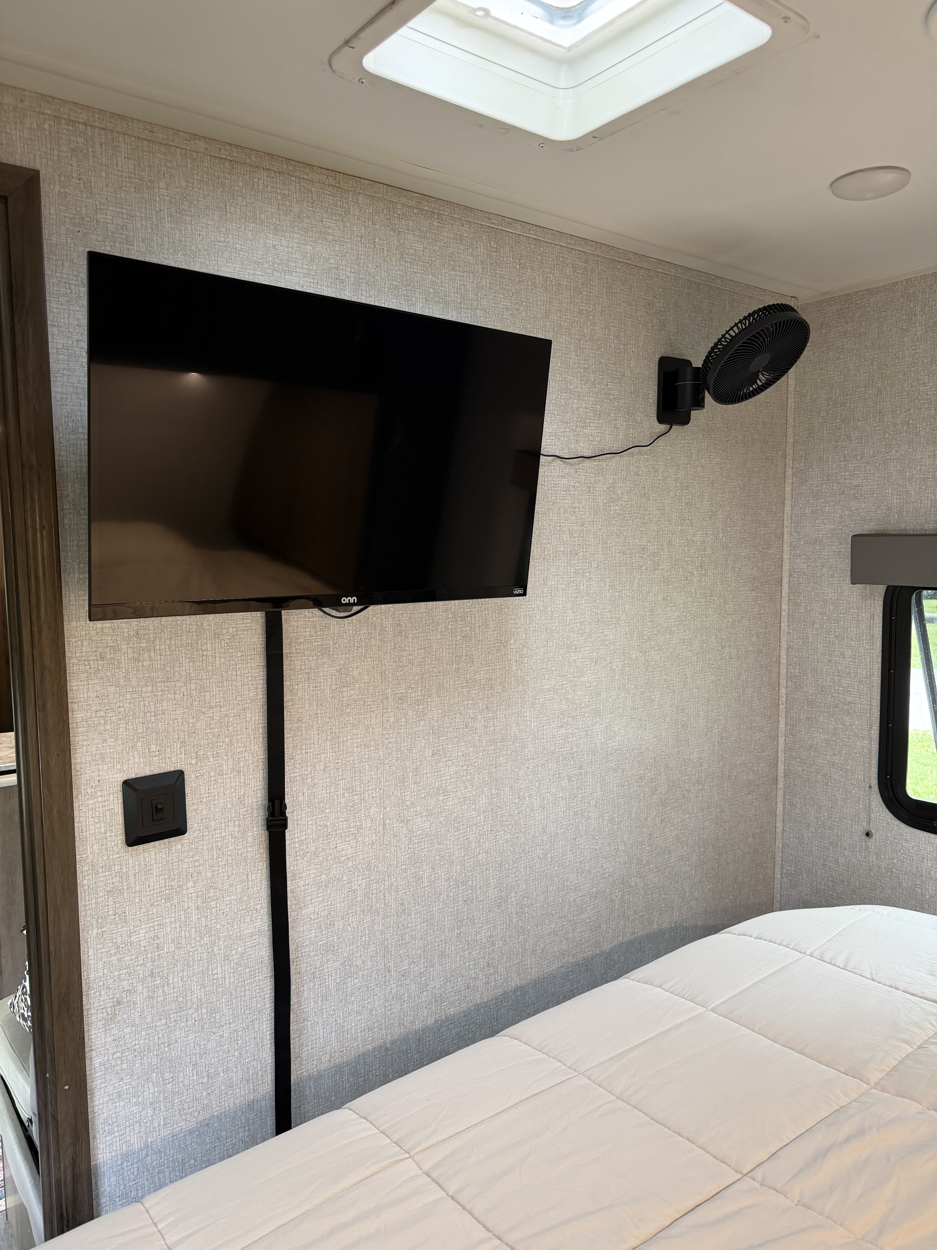 RV rental bedroom setup with a flat-screen TV, wall fan, comfy bed, and skylight for a pleasant travel stay.. East to West Silver Lake 2021