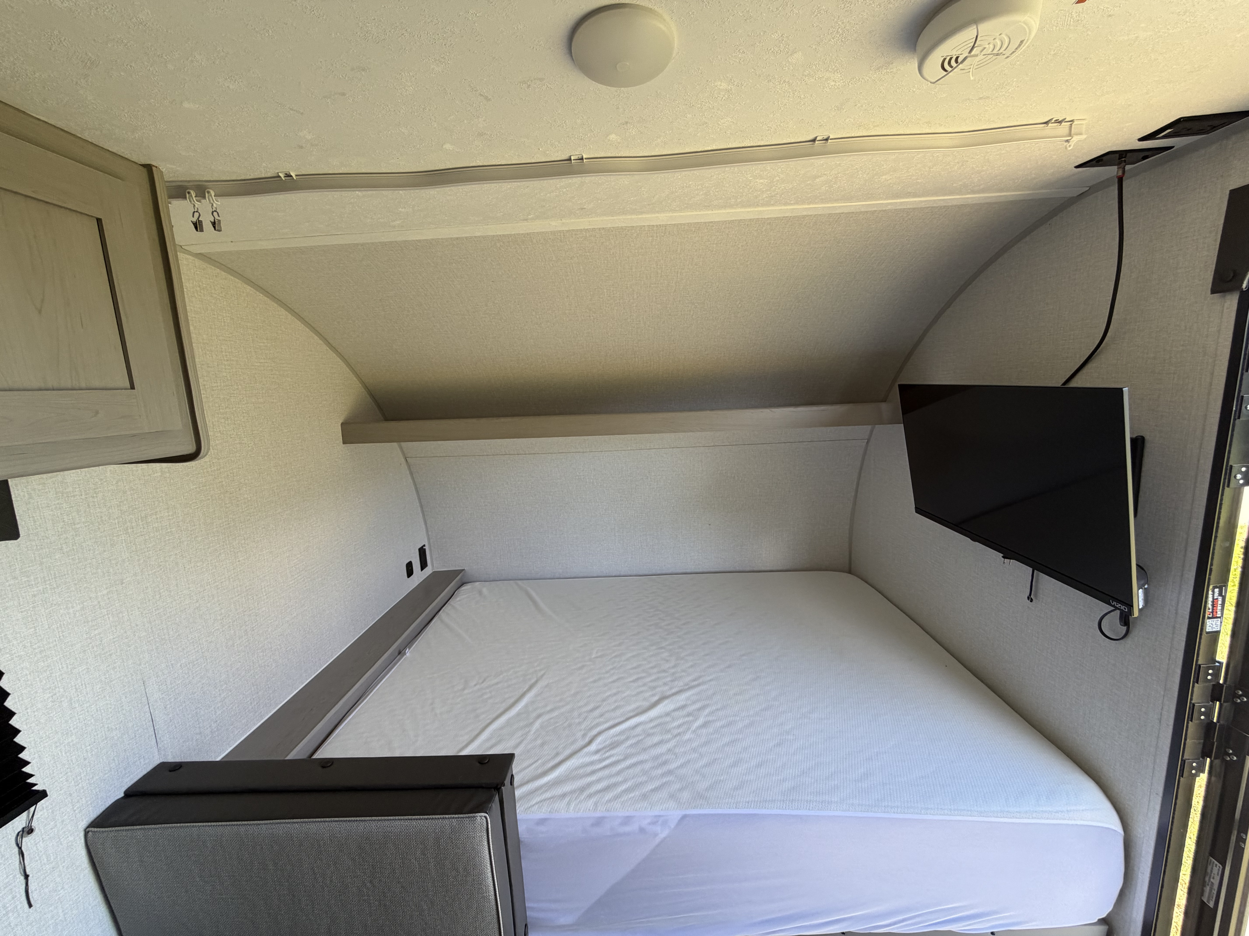 Bright RV rental sleeping area features a white mattress, wall-mounted TV, and a ceiling curtain track.. Coachmen Clipper 17CBH 2024