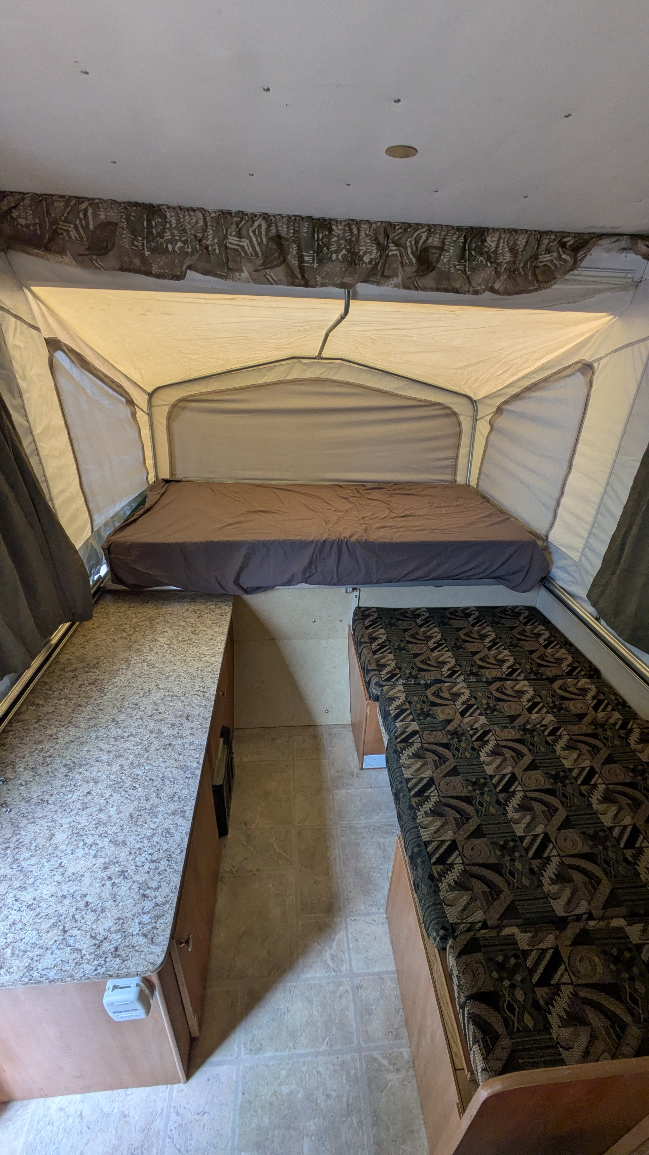Inside an rv rental pop-up camper featuring a bed, patterned bench/bed, and countertop. Ideal for camping trips.. Starcraft Starcraft Popup Trailer 2006