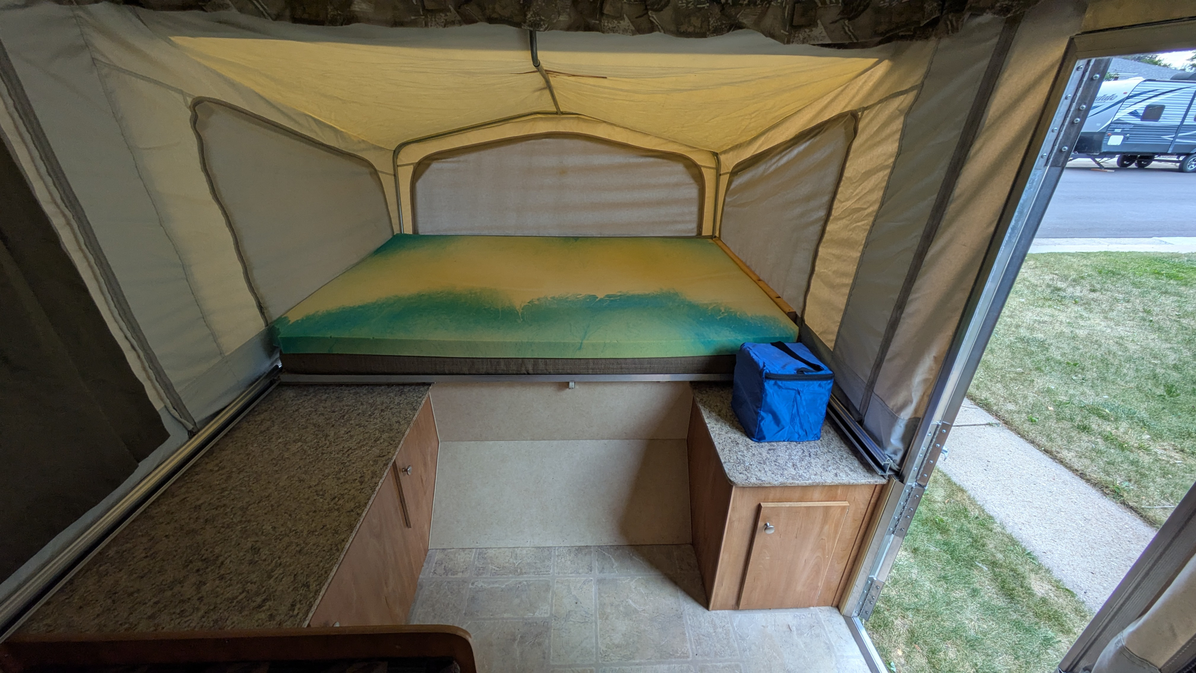 This rv rental's pop-up interior shows a bed with a vibrant yellow and green mattress, built-in storage cabinets, and fabric walls.. Starcraft Starcraft Popup Trailer 2006