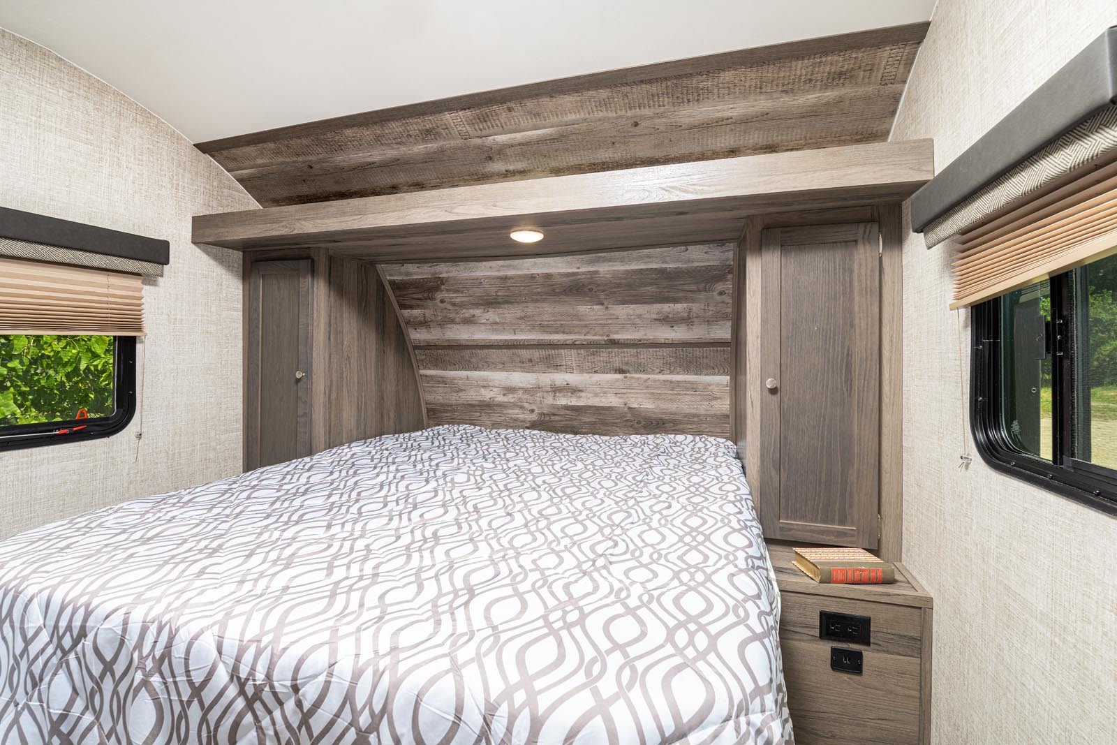 Cozy RV rental bedroom features a comfortable bed, wood-paneled headboard, and convenient bedside storage cabinets.. Gulf Stream Envision 2026