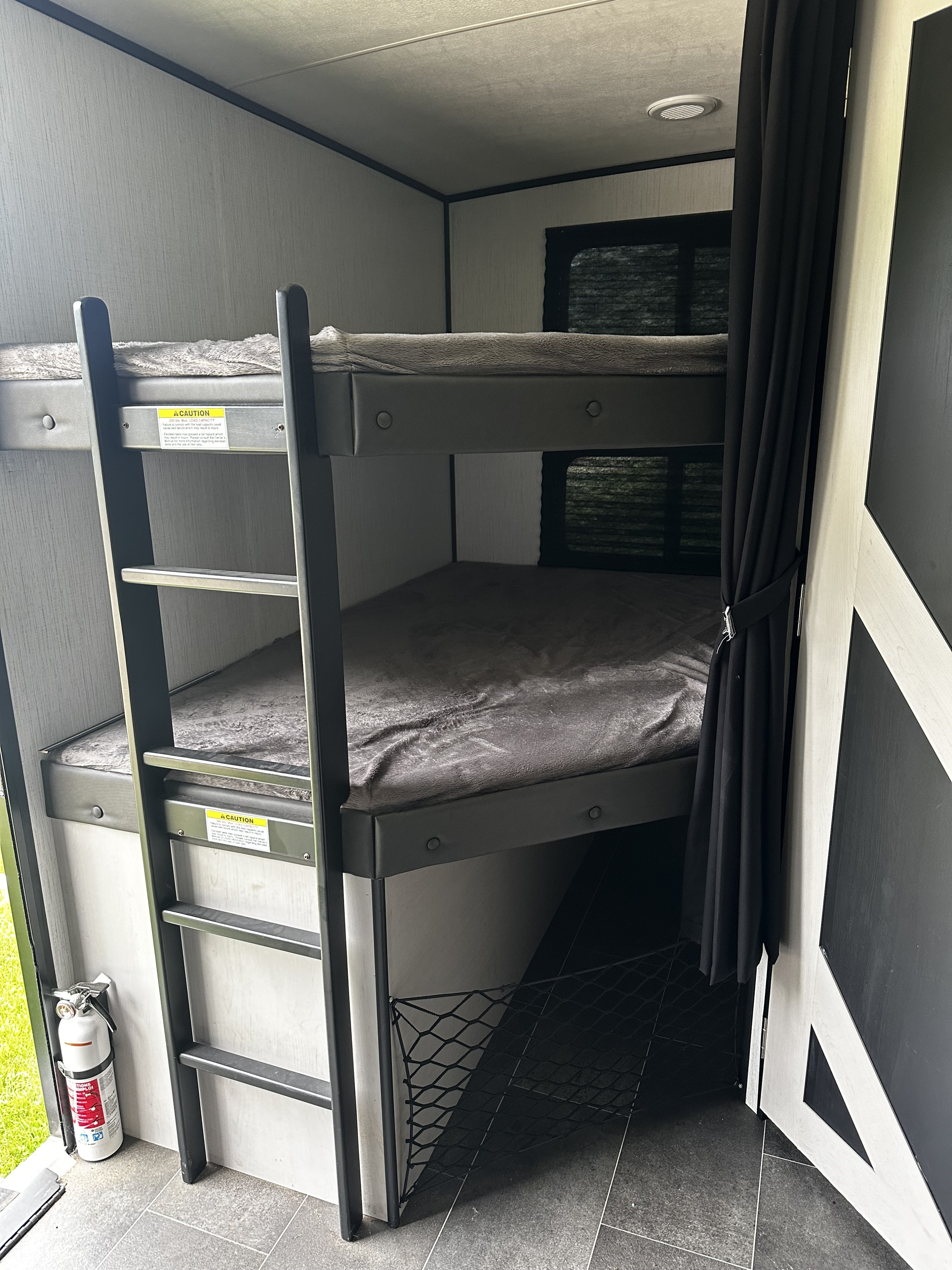 RV rental bunk beds featuring a safety ladder, cozy bedding, a fire extinguisher, and convenient storage netting.. Heartland RVs Mallard 2022