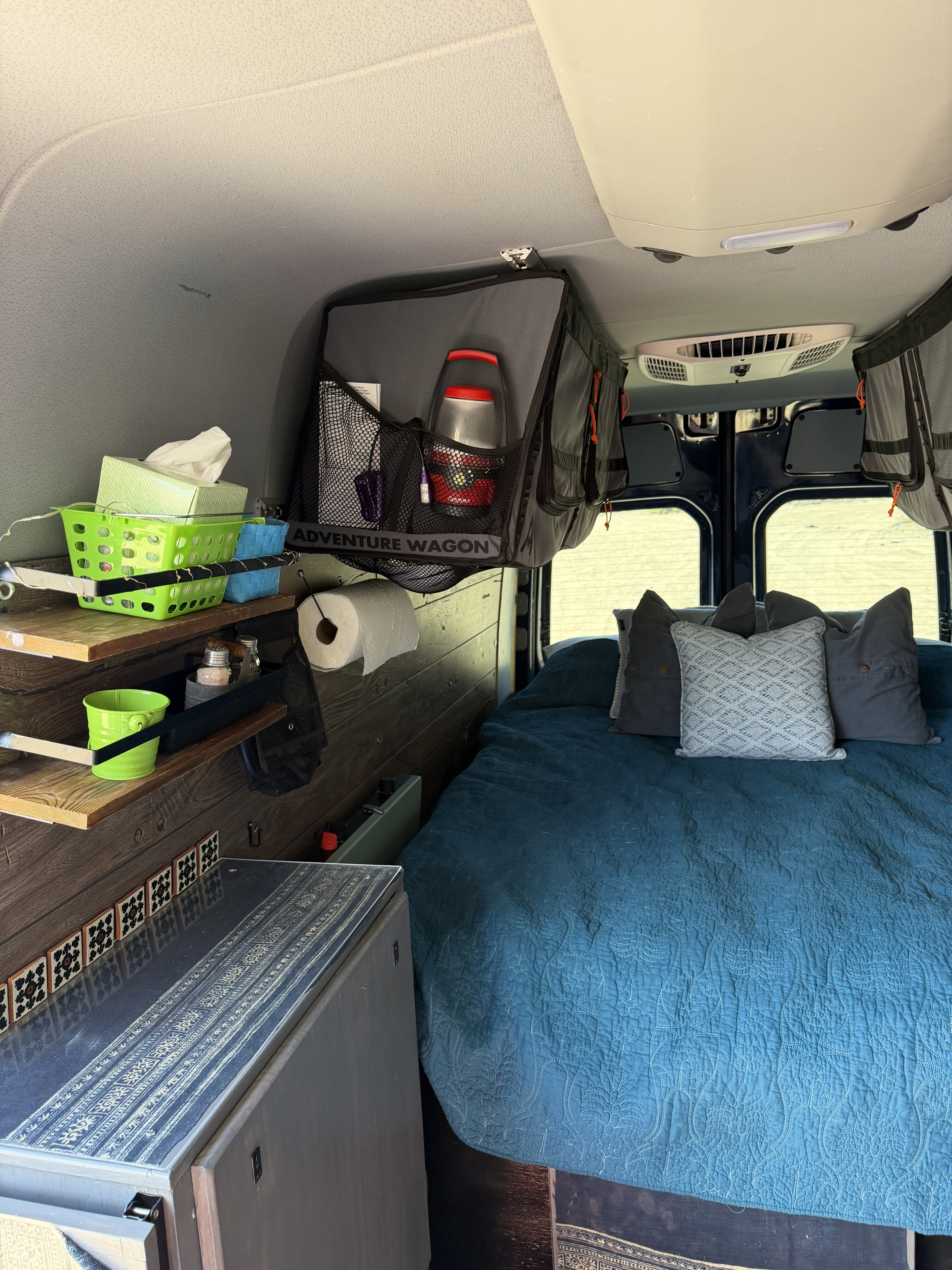 Comfortable RV rental sleeping area with a blue quilted bed, functional shelves, and overhead storage.. Mercedes-Benz Sprinter RV Motorhome Campervan 2016
