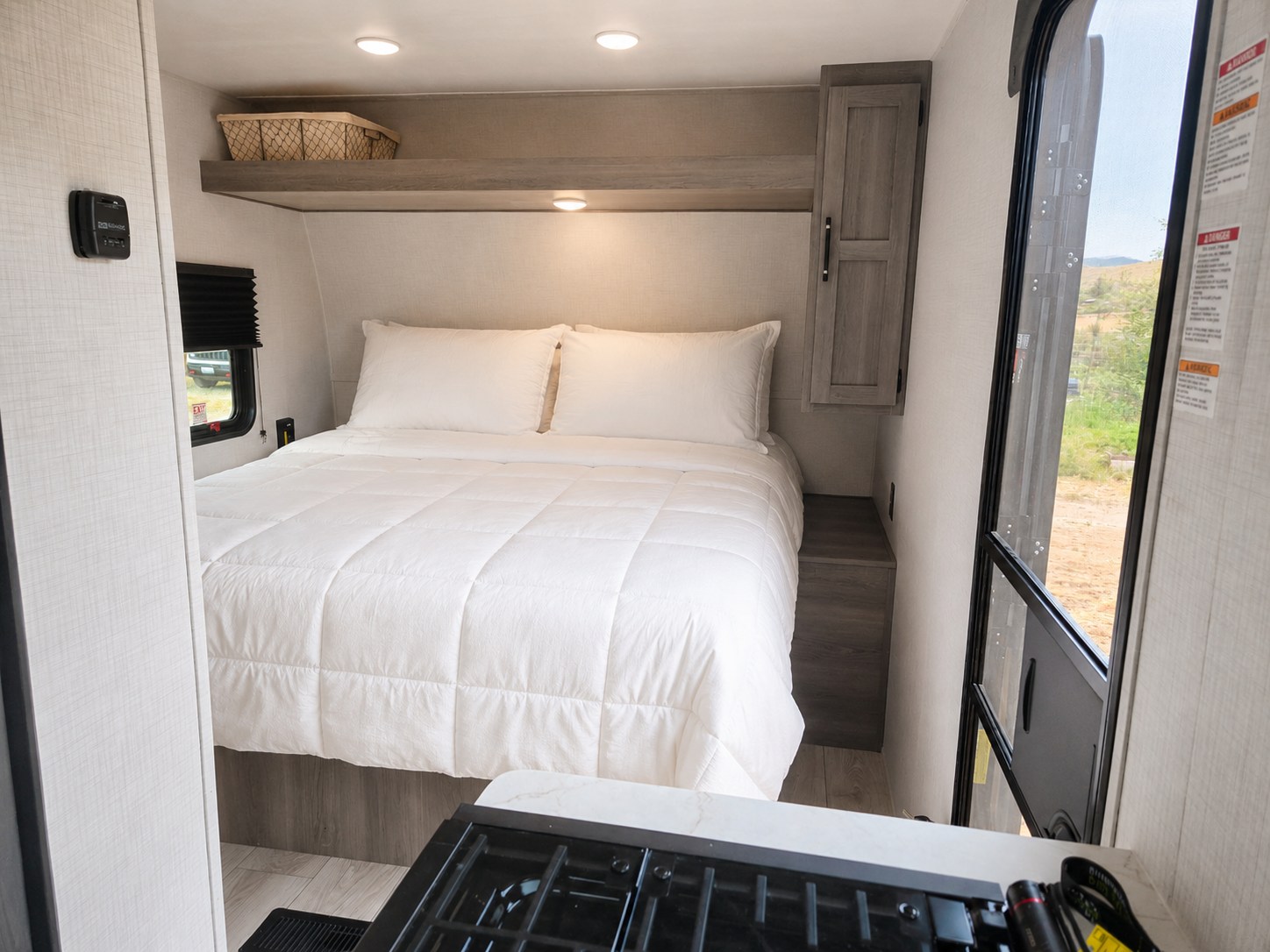 This RV rental's cozy interior features a bright bedroom with a large bed, storage, and a compact kitchen stove in view.. Keystone RV Hideout sport 200rlwe 2026