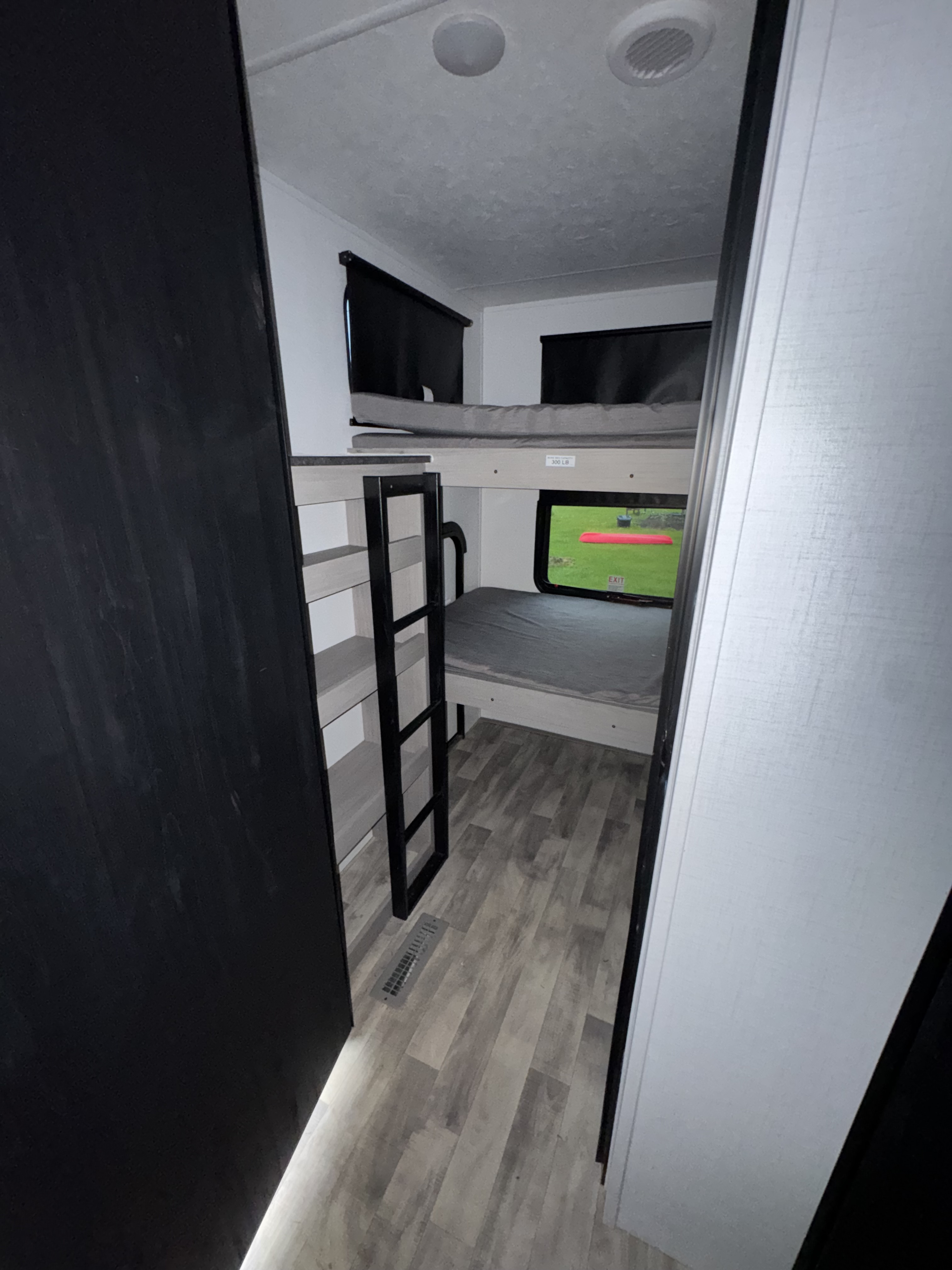 Inside this rv rental, a compact bunk bed area with gray mattresses, a ladder, and a window showing a green outdoor view.. Dutchmen Kodiak Ultra Lite 2024