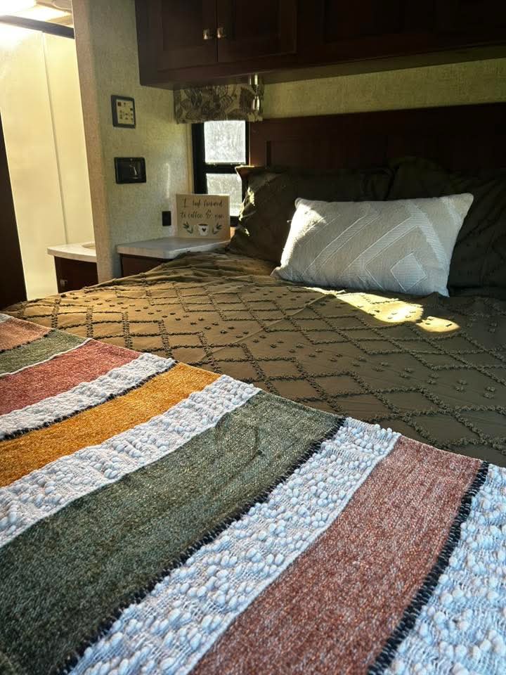 Cozy RV rental bedroom with olive green bedding, white pillow, and a colorful striped blanket at the foot of the bed.. Forest River Ford 2019