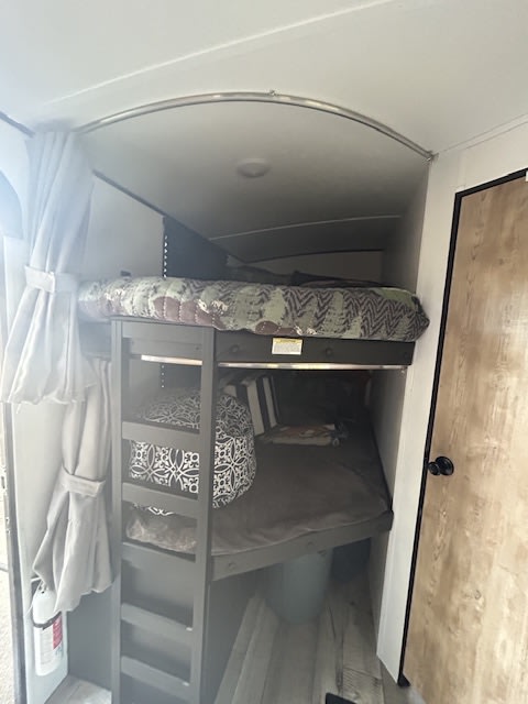 Cozy RV rental bunk beds. This camper interior offers a compact sleeping area with privacy curtains and a ladder.. Keystone RV Springdale 2022