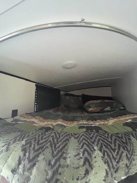Cozy RV rental bedroom with a low, curved ceiling, recessed light, and a bed featuring green and camouflage-patterned bedding.. Keystone RV Springdale 2022