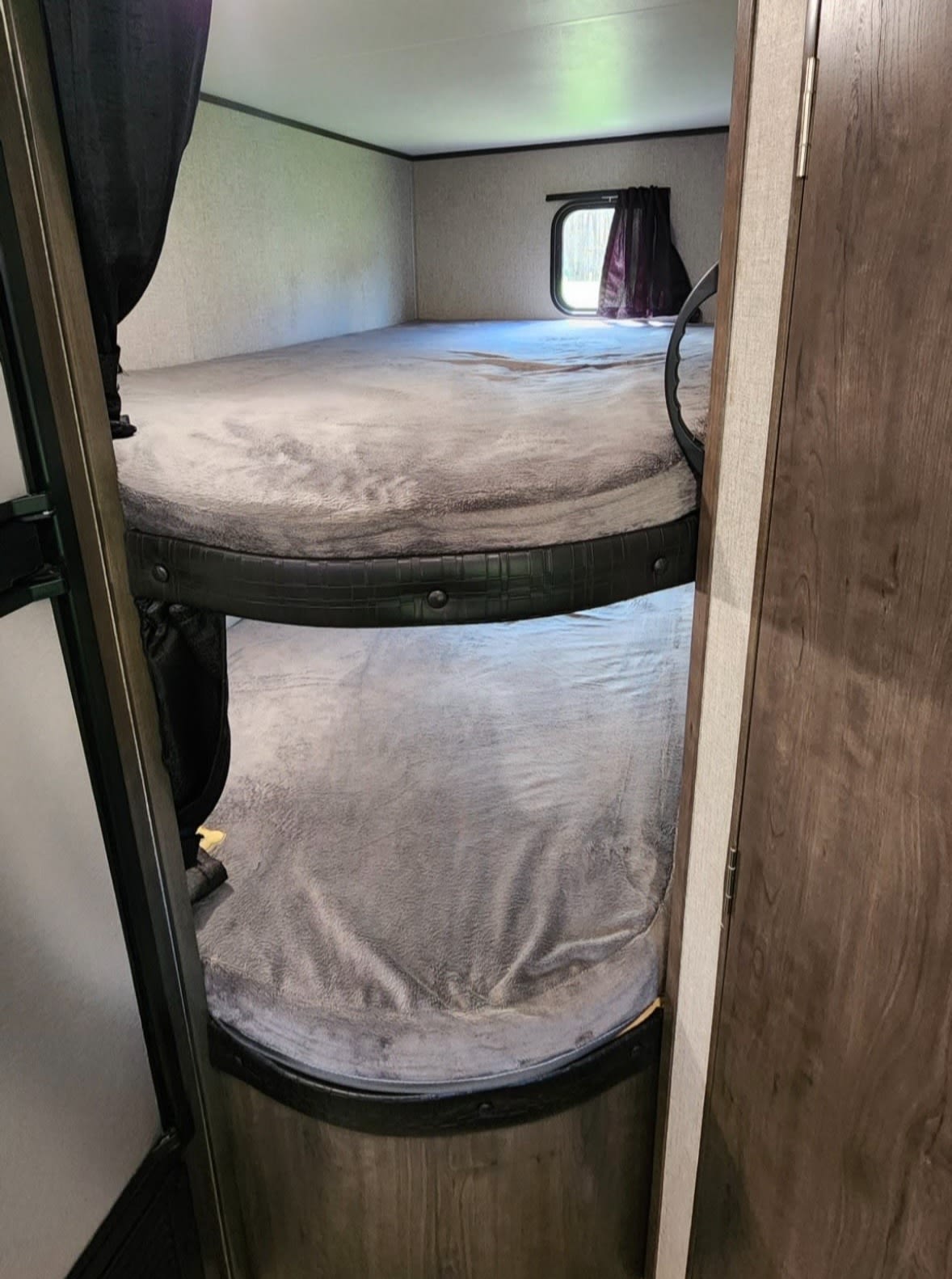 Cozy RV rental bunk beds with soft grey bedding, a small window with curtains, and dark privacy curtains, ready for guests.. Jayco Jay Flight SLX 2021