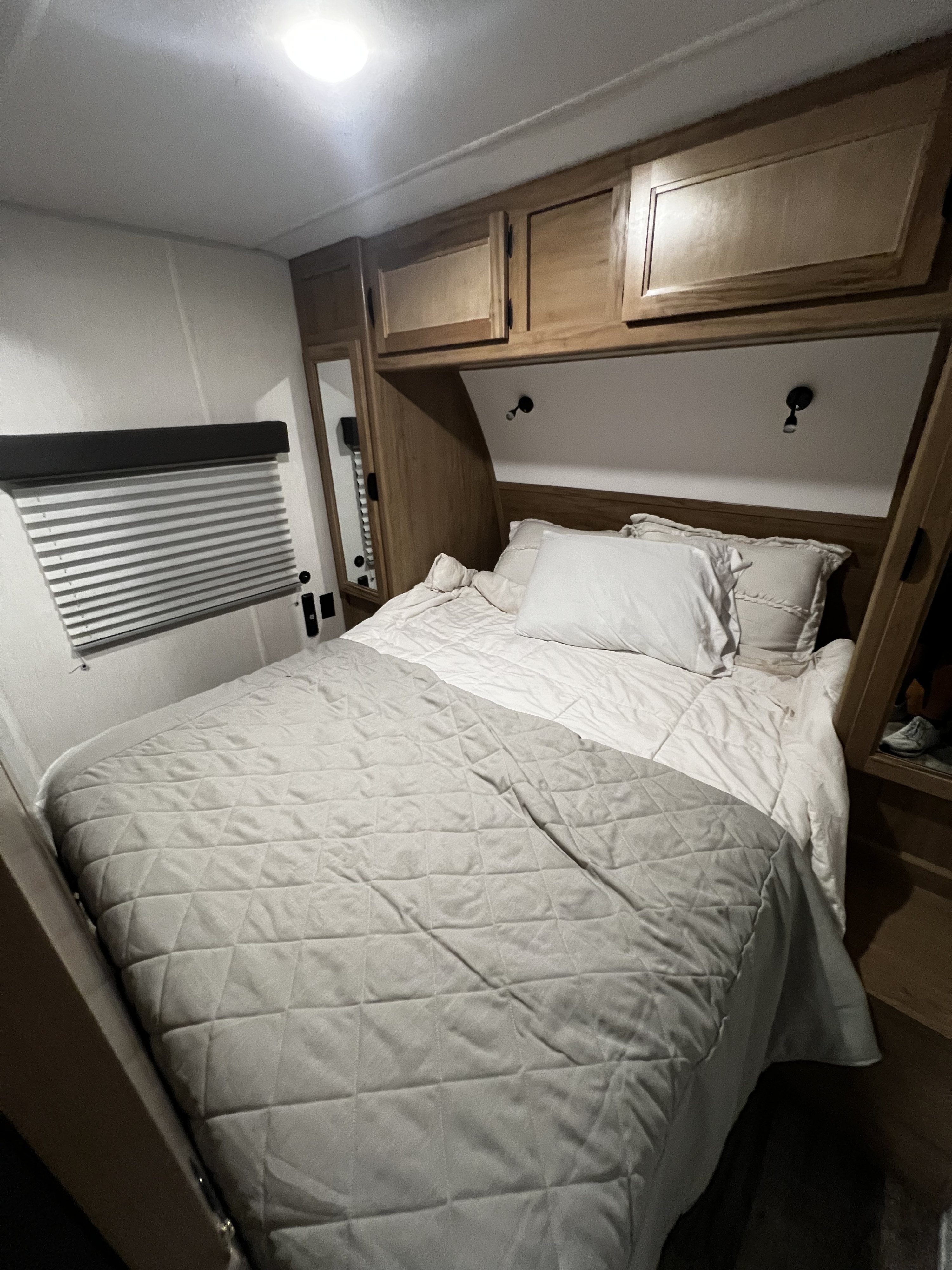 Cozy RV rental bedroom with compact bed, light bedding, overhead cabinets, and window blinds, ideal for a camper stay.. Forest River Cherokee Grey Wolf Black Label 2024