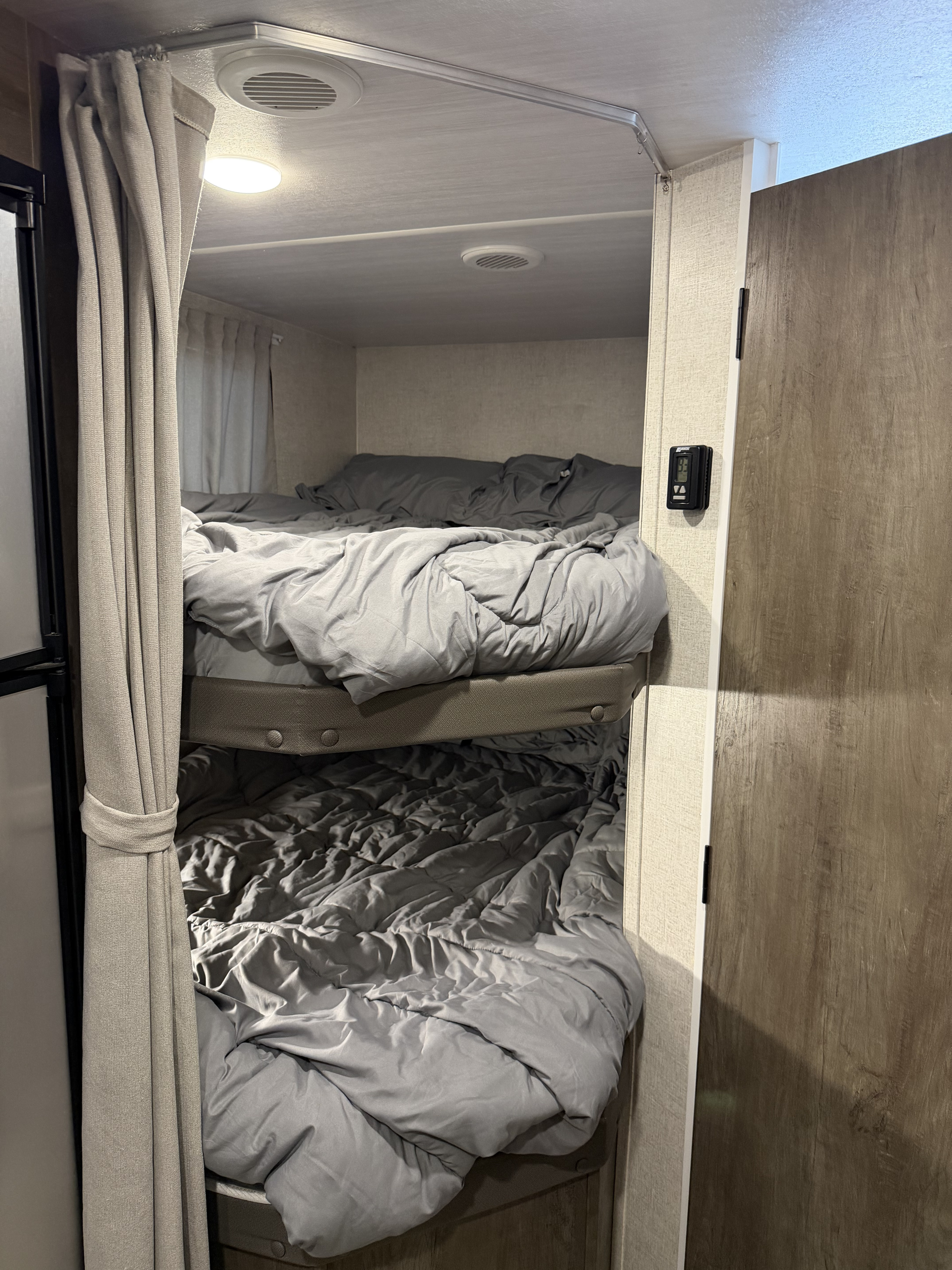 Inside an RV rental: two cozy bunk beds with gray bedding and a privacy curtain. Note the thermostat and ceiling vents.. Forest River Salem Cruise Lite 2021
