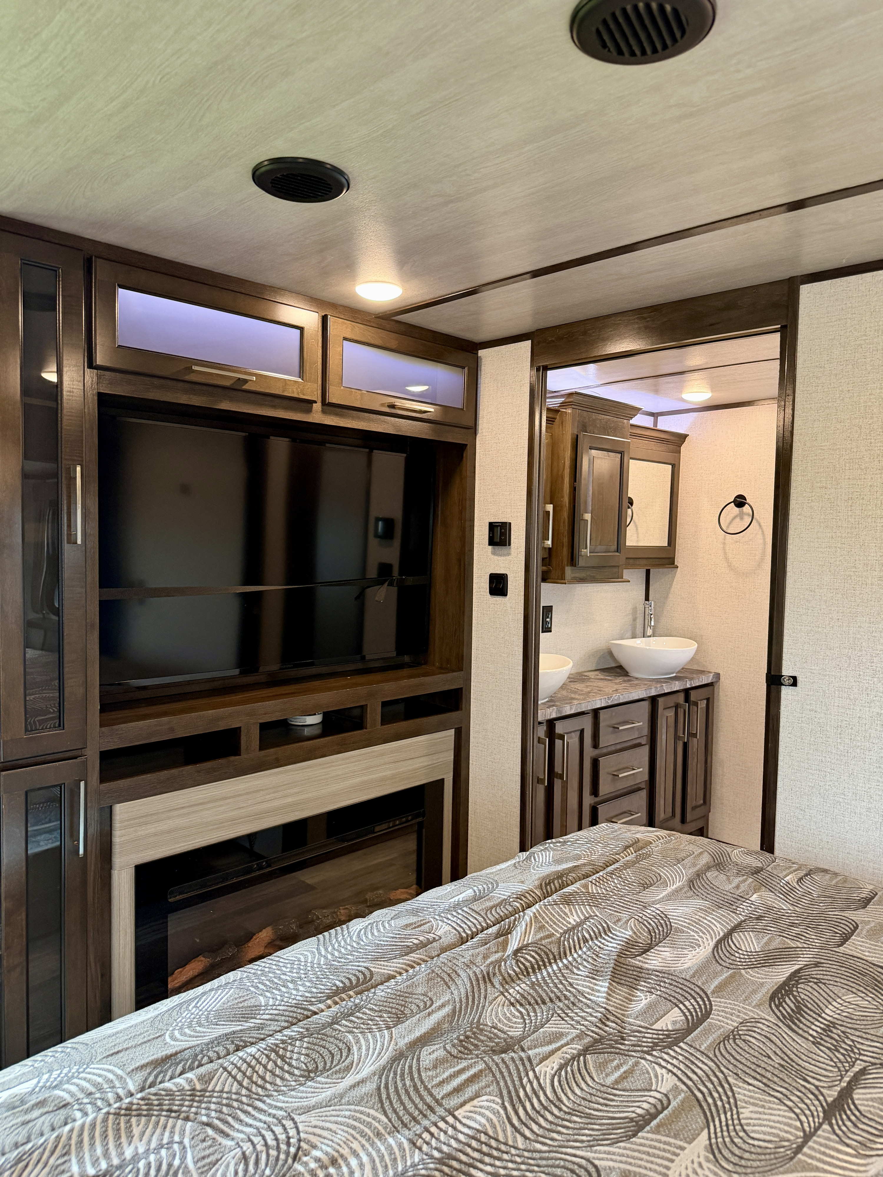 Inside an RV rental: a cozy bedroom features a TV, fireplace, and an adjoining bathroom with double sinks.. Dutchmen Yukon 2021
