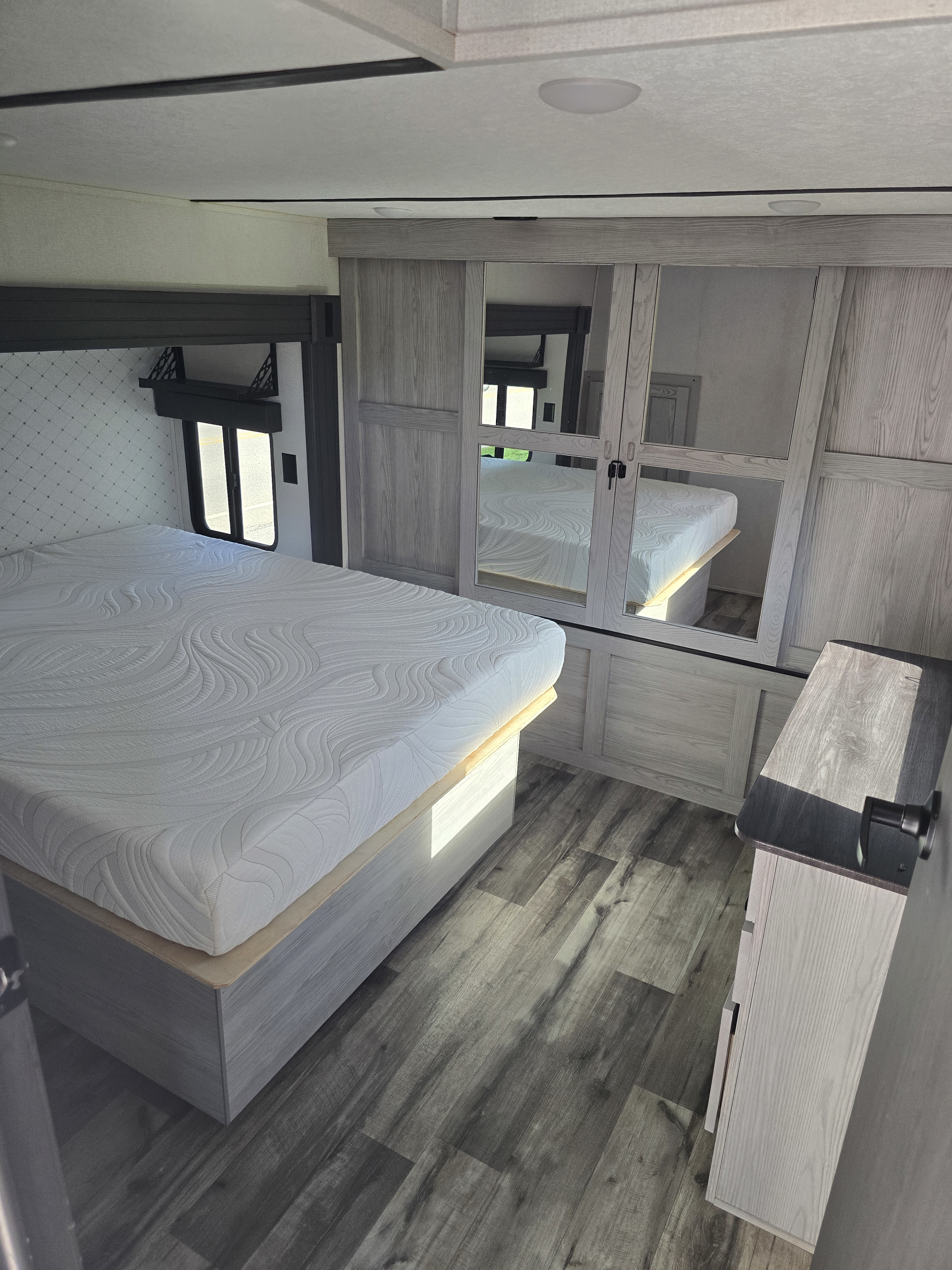 This RV rental bedroom features a comfortable bed, mirrored closet, and wood-look flooring, offering cozy travel accommodations.. Keystone RV Montana High Country 2022