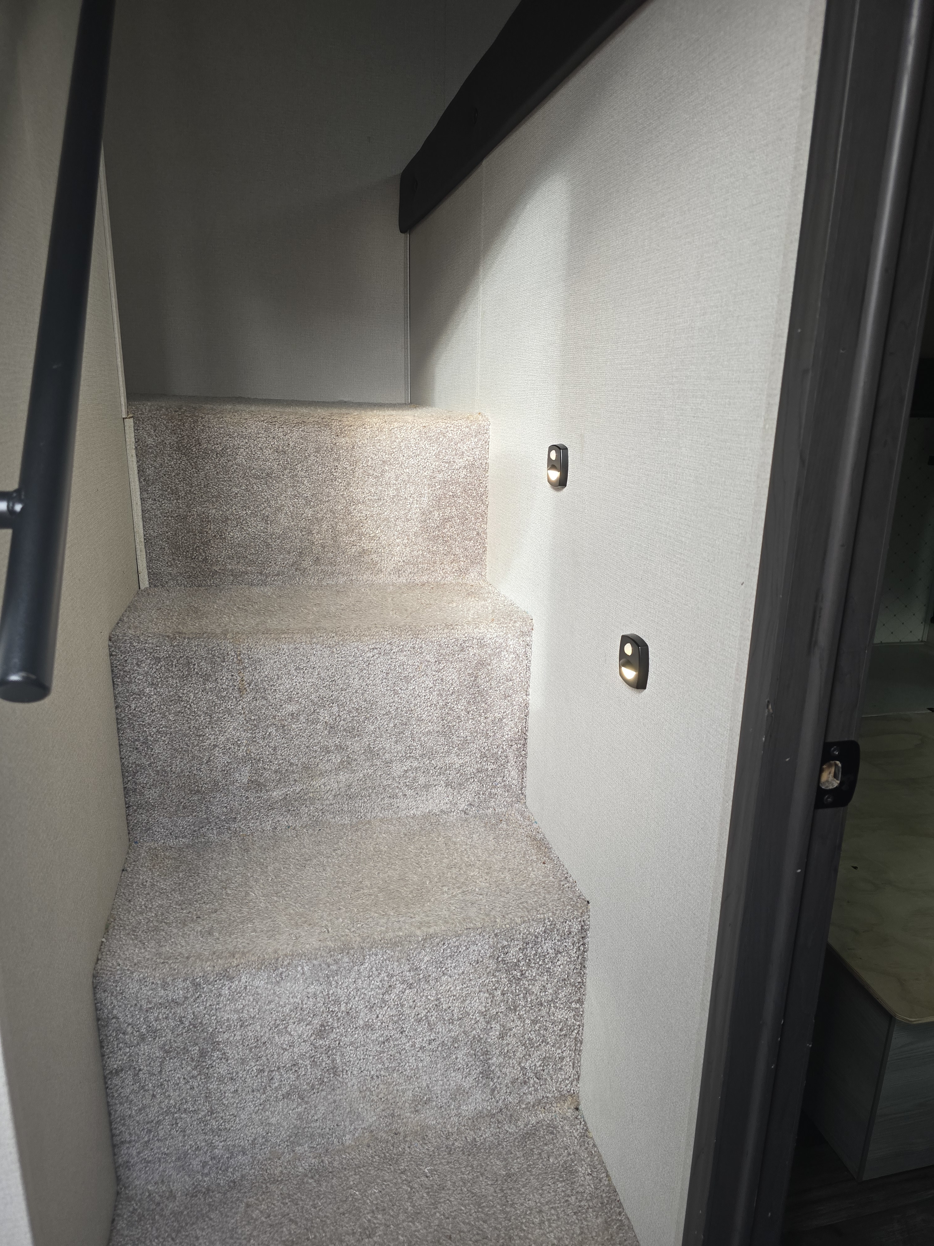 Carpeted RV rental interior staircase with subtle wall lighting and a handrail, guiding users upstairs within the RV.. Keystone RV Montana High Country 2022