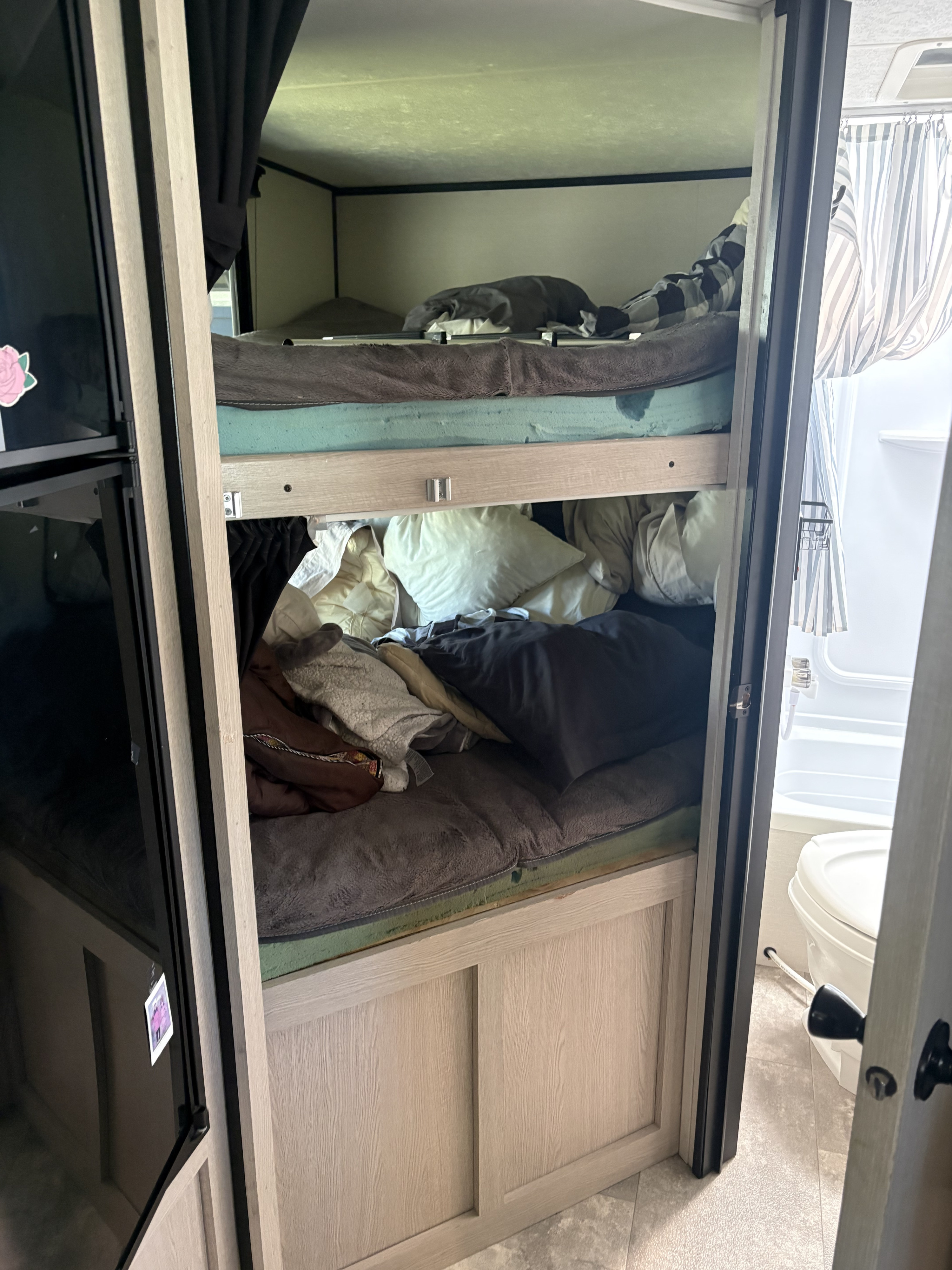 Cozy RV rental interior with bunk beds, blankets, and a glimpse of the small bathroom. Perfect for family adventures.. Coachmen Apex 2022