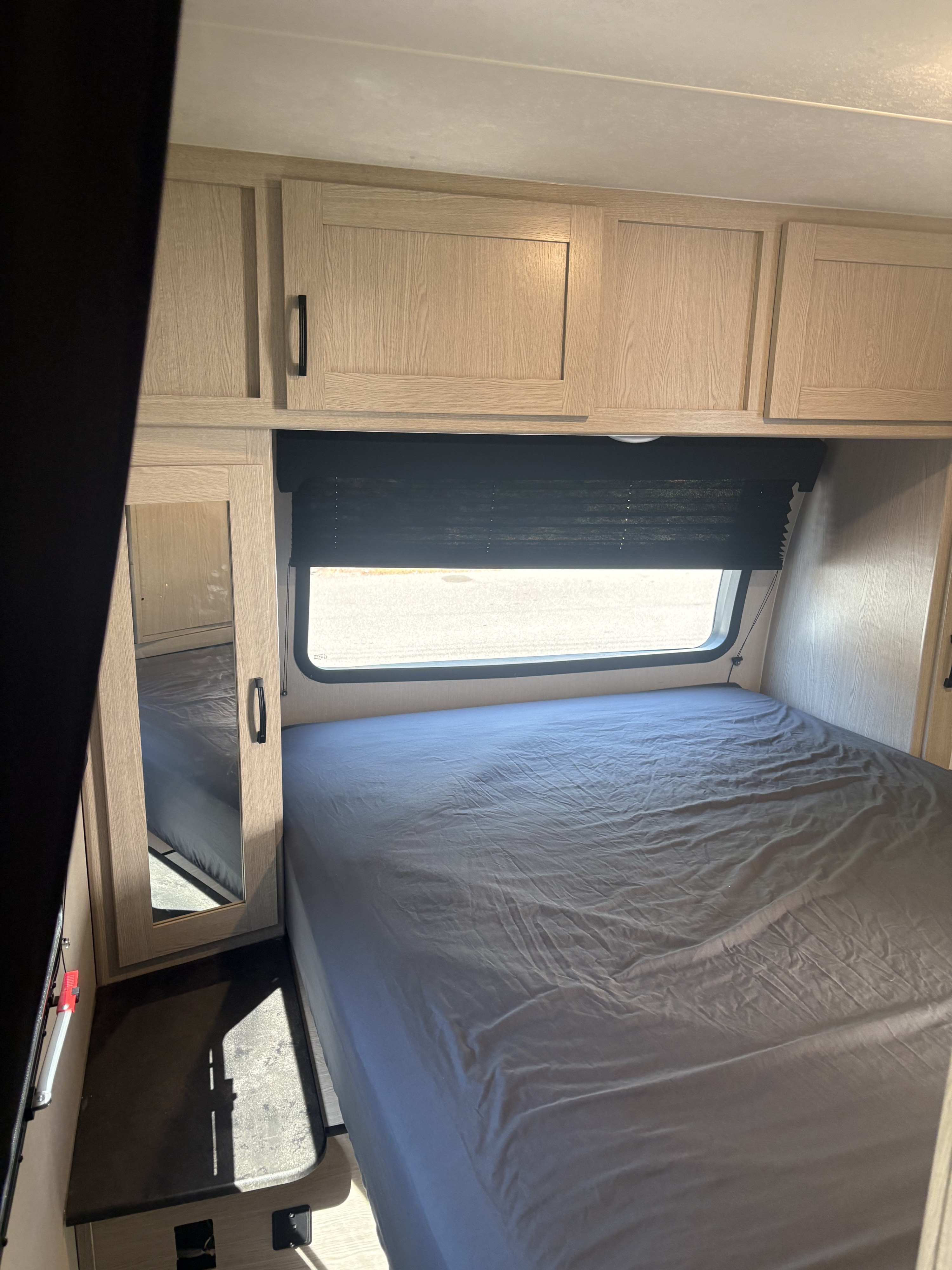 RV rental bedroom interior: grey bed, overhead wood cabinets, window with blind, & mirrored door. Compact, comfy space.. Coachmen Apex 2022