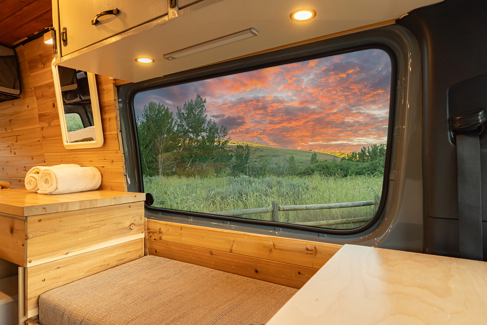 Experience stunning sunsets from this cozy RV rental. Custom van interior with a window overlooking a vibrant, green landscape.. MERCEDES-BENZ SPRINTER 2500 170 WB 2022