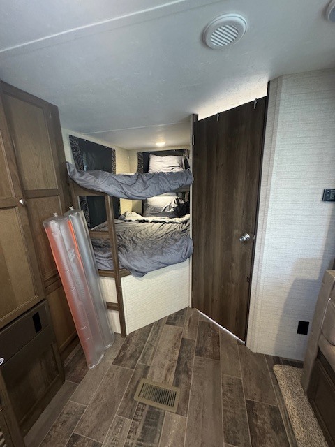 RV rental interior: bunk beds with grey bedding, wood cabinets, and an inflatable item on the wood-look floor.. Keystone RV Bullet Ultra Lite 2017