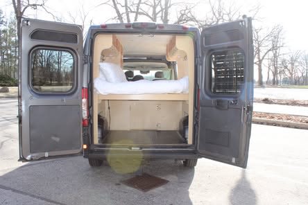 This RV rental camper van interior, with open rear doors, shows a bed with storage below, perfect for mobile living.. Dodge Ram 1500 2022