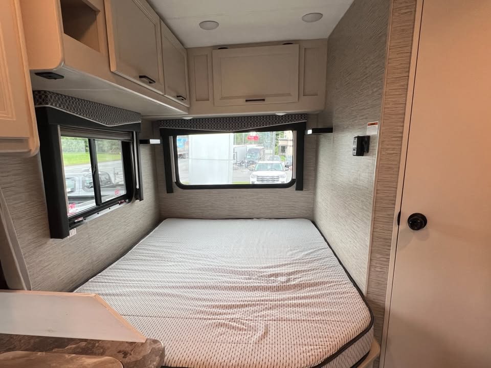 This cozy RV rental bedroom features a comfy bed, overhead cabinets, and windows, offering a peaceful retreat for your travels.. Thor Motor Coach Chateau 2022