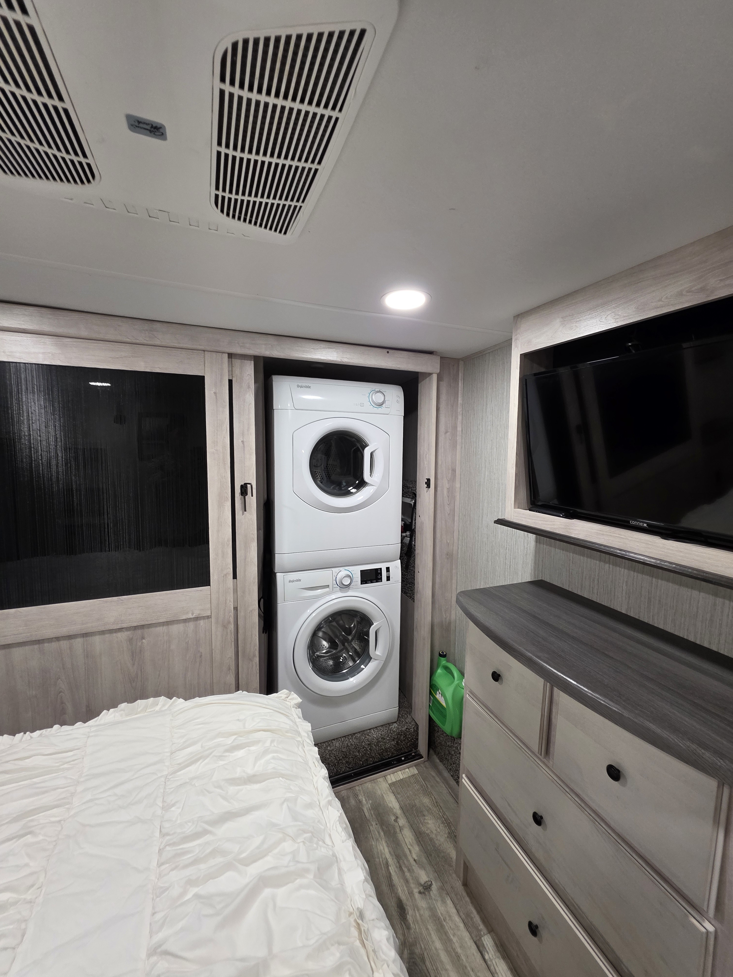 Inside a modern RV rental: a compact bedroom with stacked laundry appliances, a comfy bed, and a TV for your journeys.. Forest River Sandpiper 2022