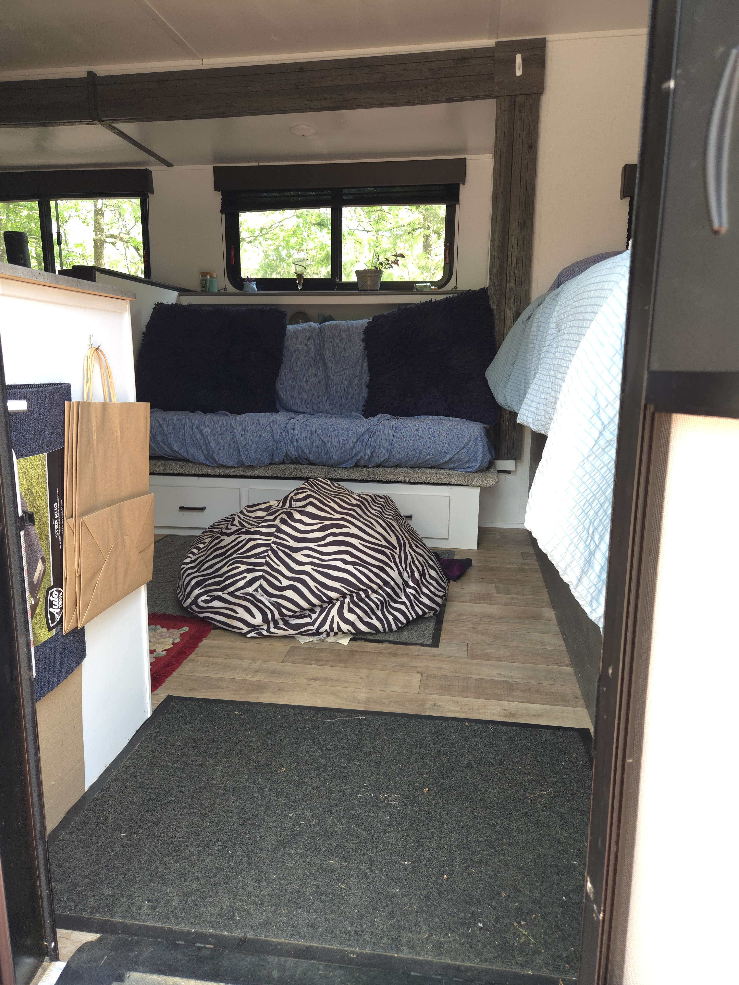 Cozy rv rental interior, showing a blue couch, zebra beanbag on the floor, and a bed with light blue bedding from the entrance.. Keystone RV Hideout 2022
