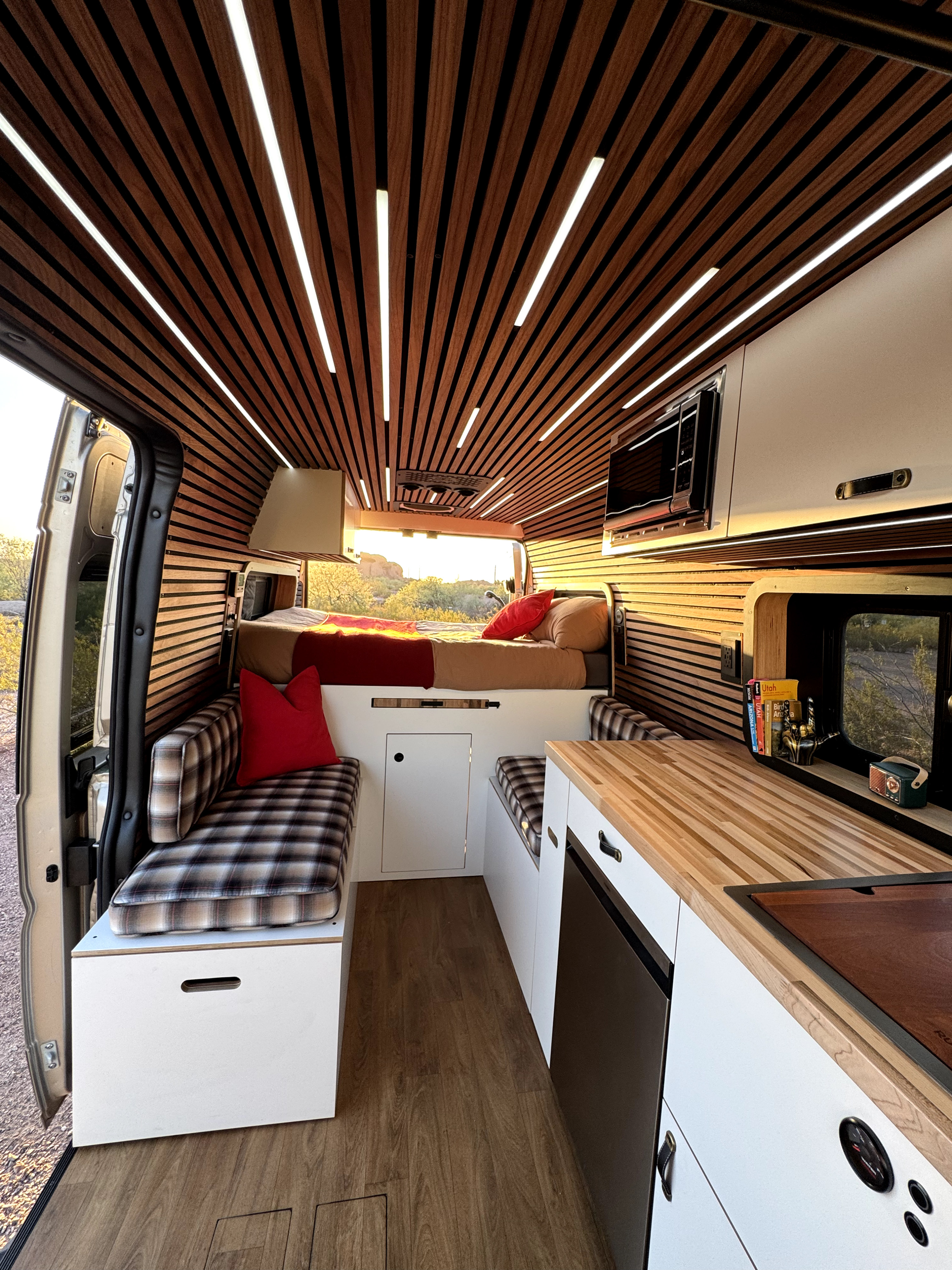 Stylish RV rental interior with a wood slat ceiling, LED lighting, compact kitchen, bed, and plaid seating.. Ram Promaster 2500 High Roof 2023