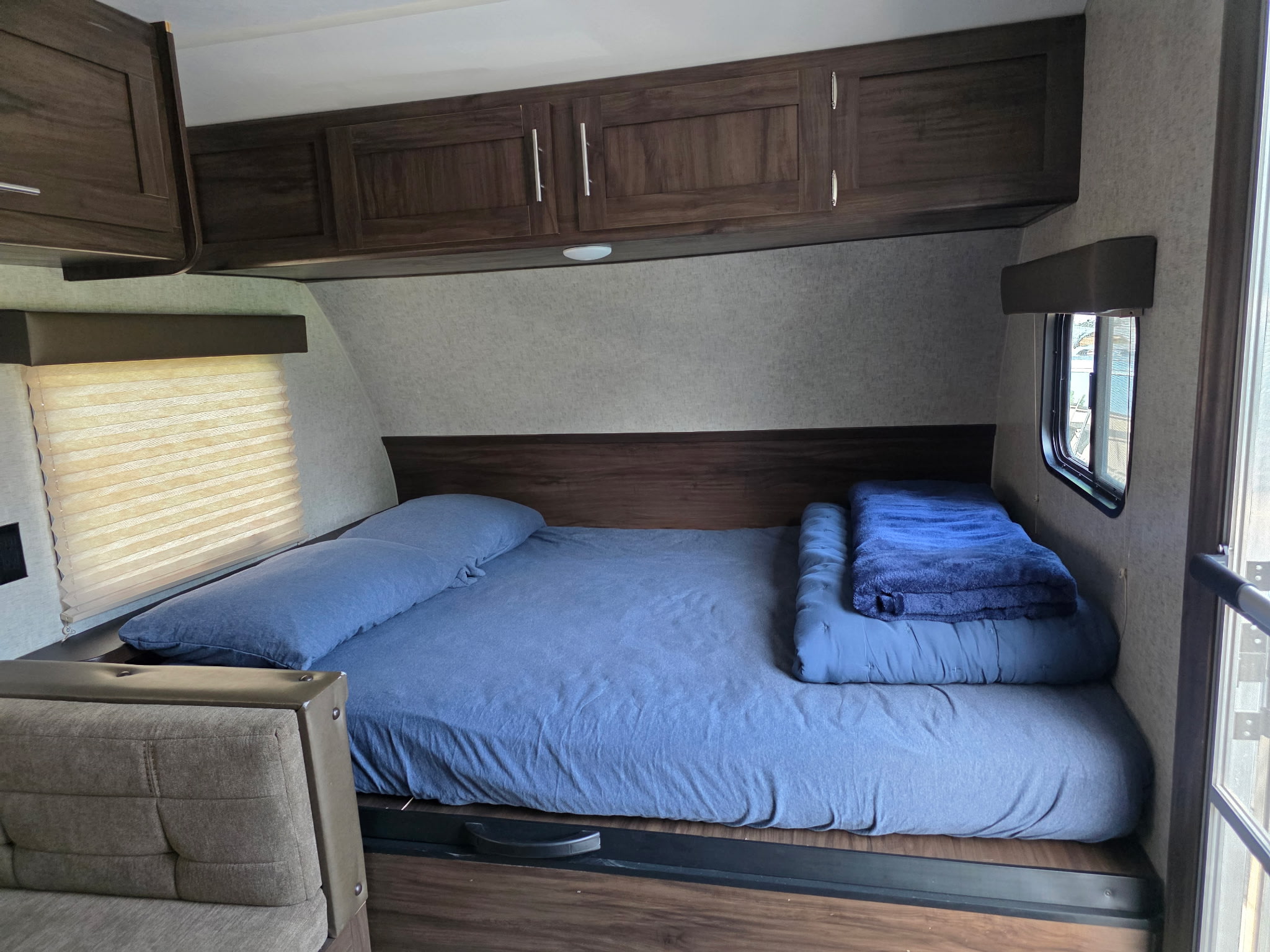 Inside this RV rental, a comfy sleeping area features blue bedding, overhead cabinets, and a window for natural light.. Forest River Cherokee Wolf Pup 2018
