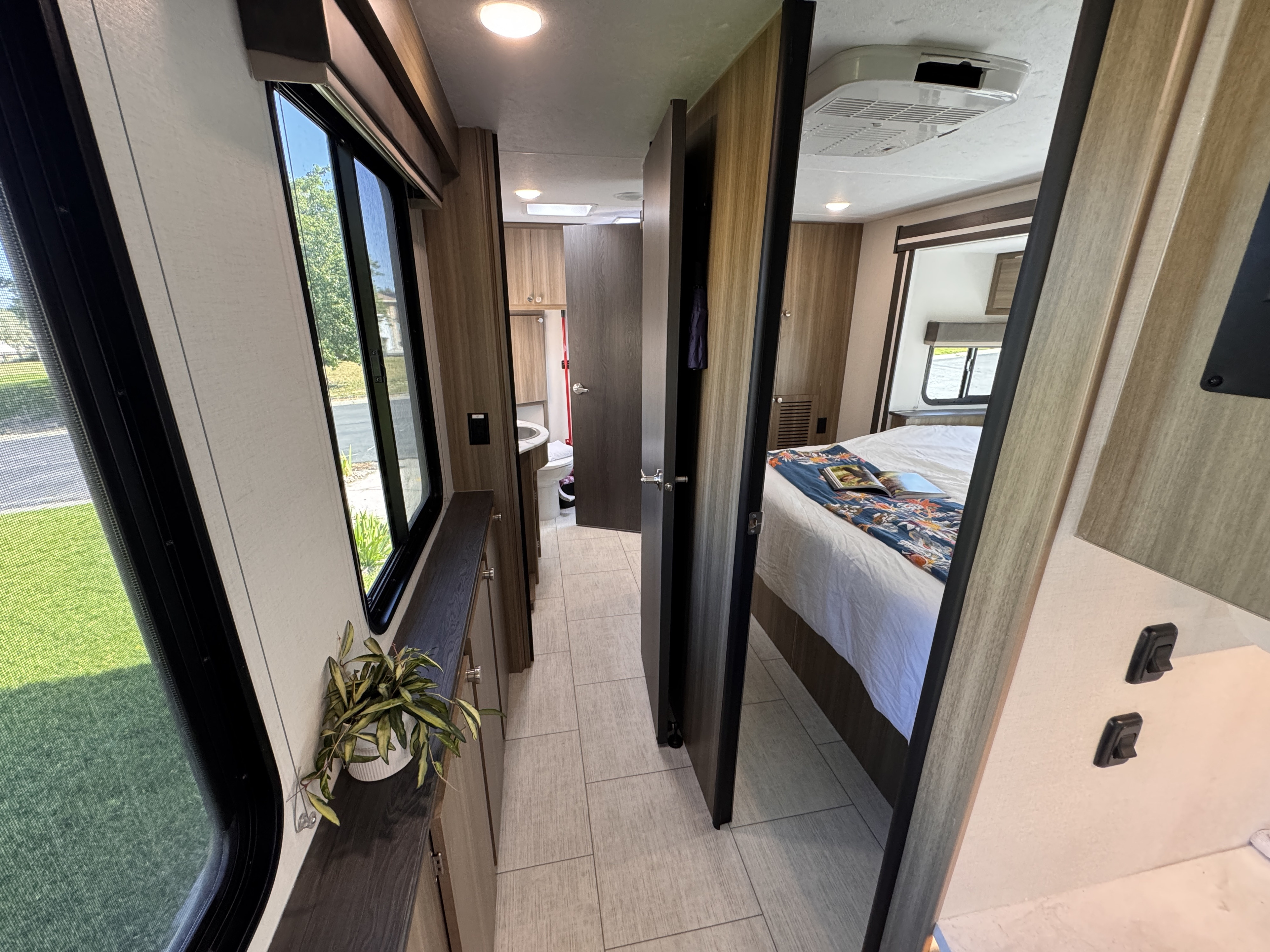 Modern RV rental interior: a hallway leads past a window with a plant, to a bright bedroom and a compact bathroom.. Forest River Coachmen Freelander 2026