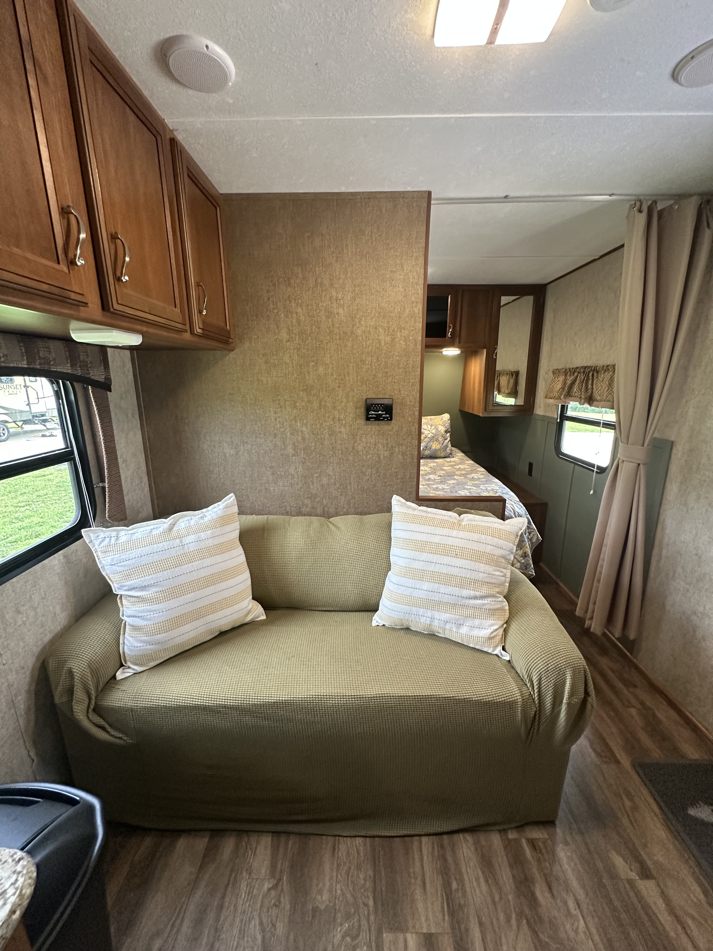 Cozy RV rental interior featuring a green sofa, striped pillows, and a peek into the bedroom with a patterned bedspread.. Avenger Avenger Trailer 2016