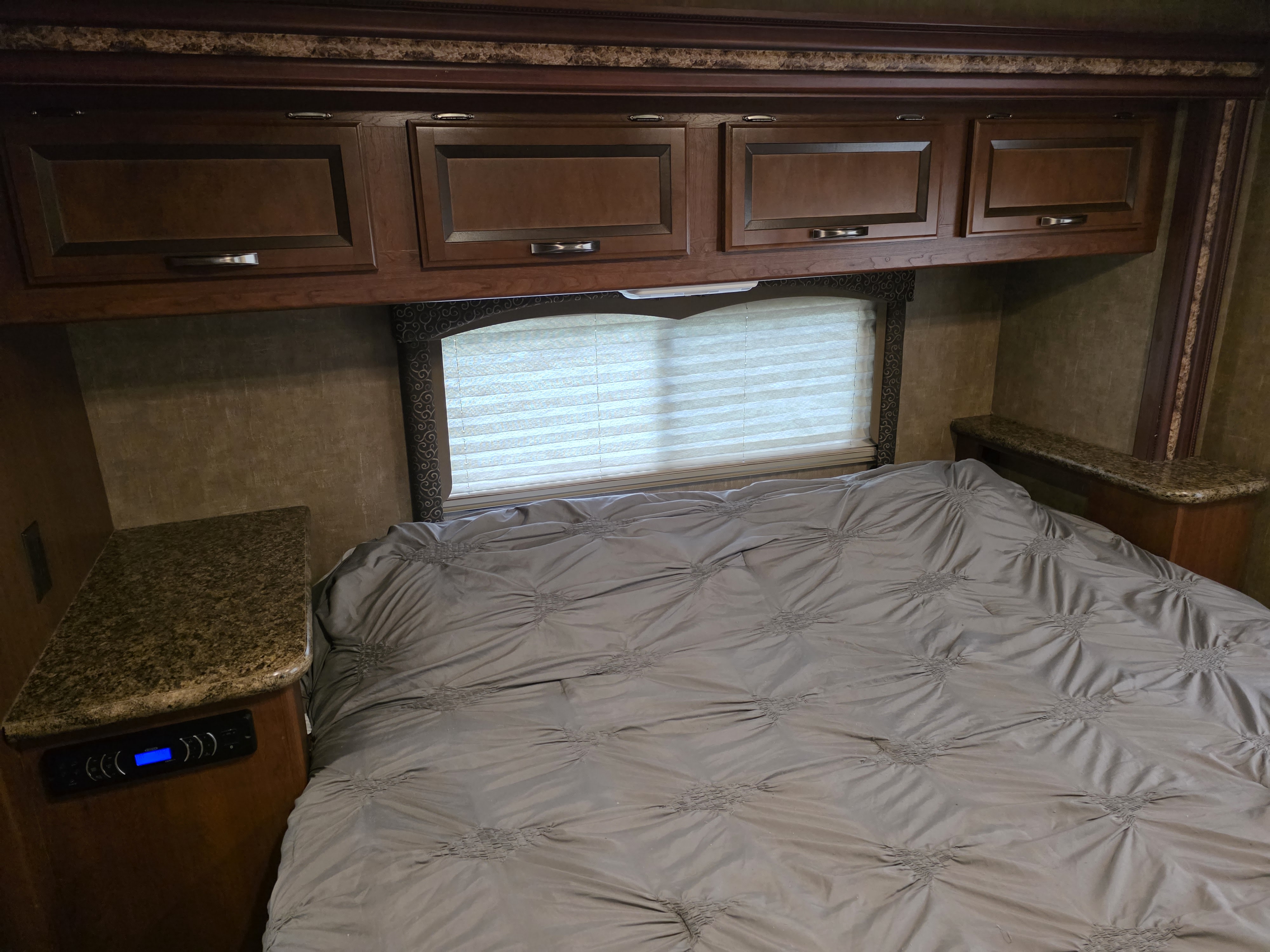 RV rental bedroom with a grey bed, overhead storage cabinets, window with blinds, and nightstands, one featuring a control panel.. Thor Four Winds 2015