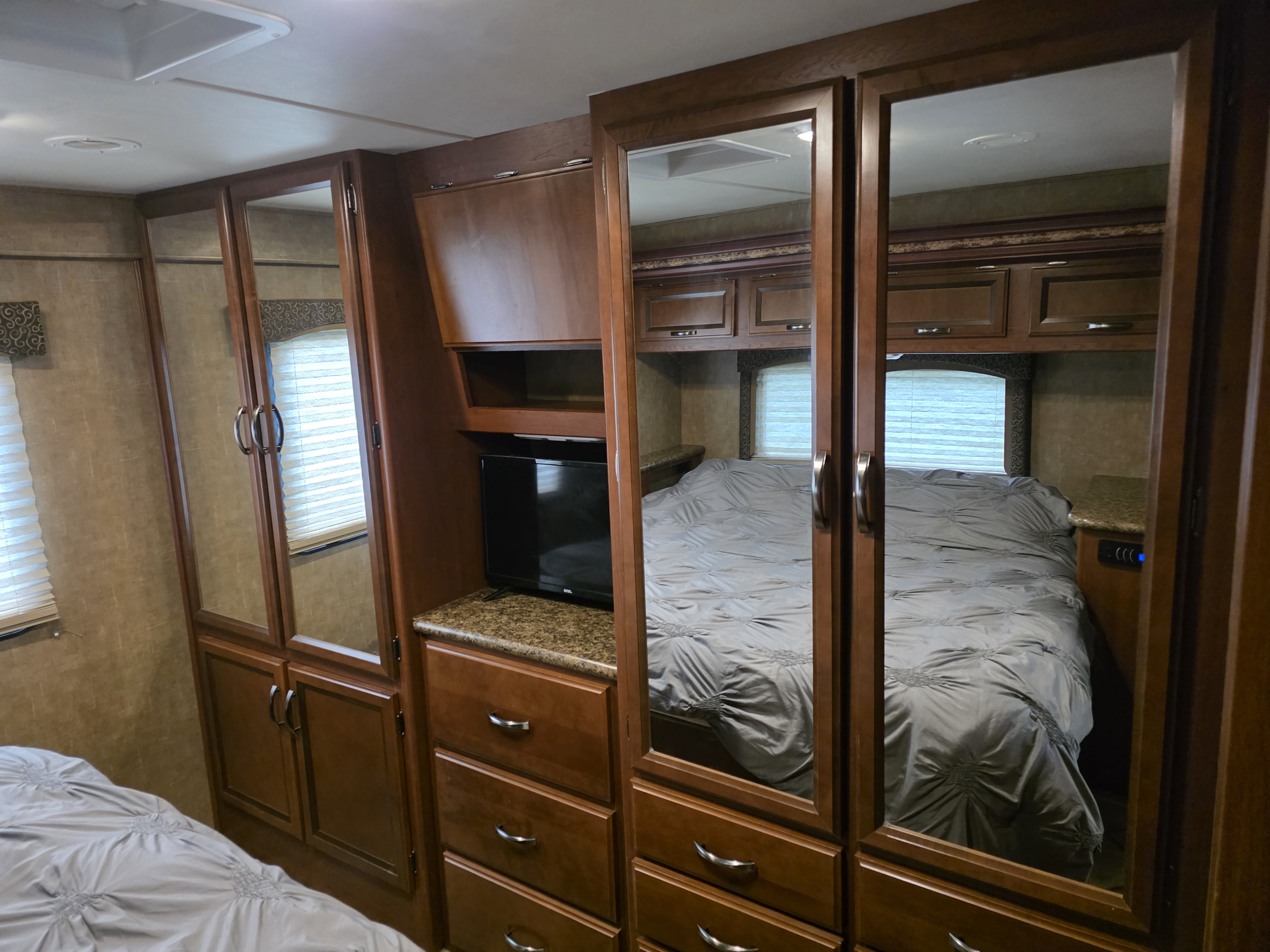 Cozy RV rental bedroom: queen bed, mirrored wardrobe, TV, and ample wood storage for comfort on the road.. Thor Four Winds 2015