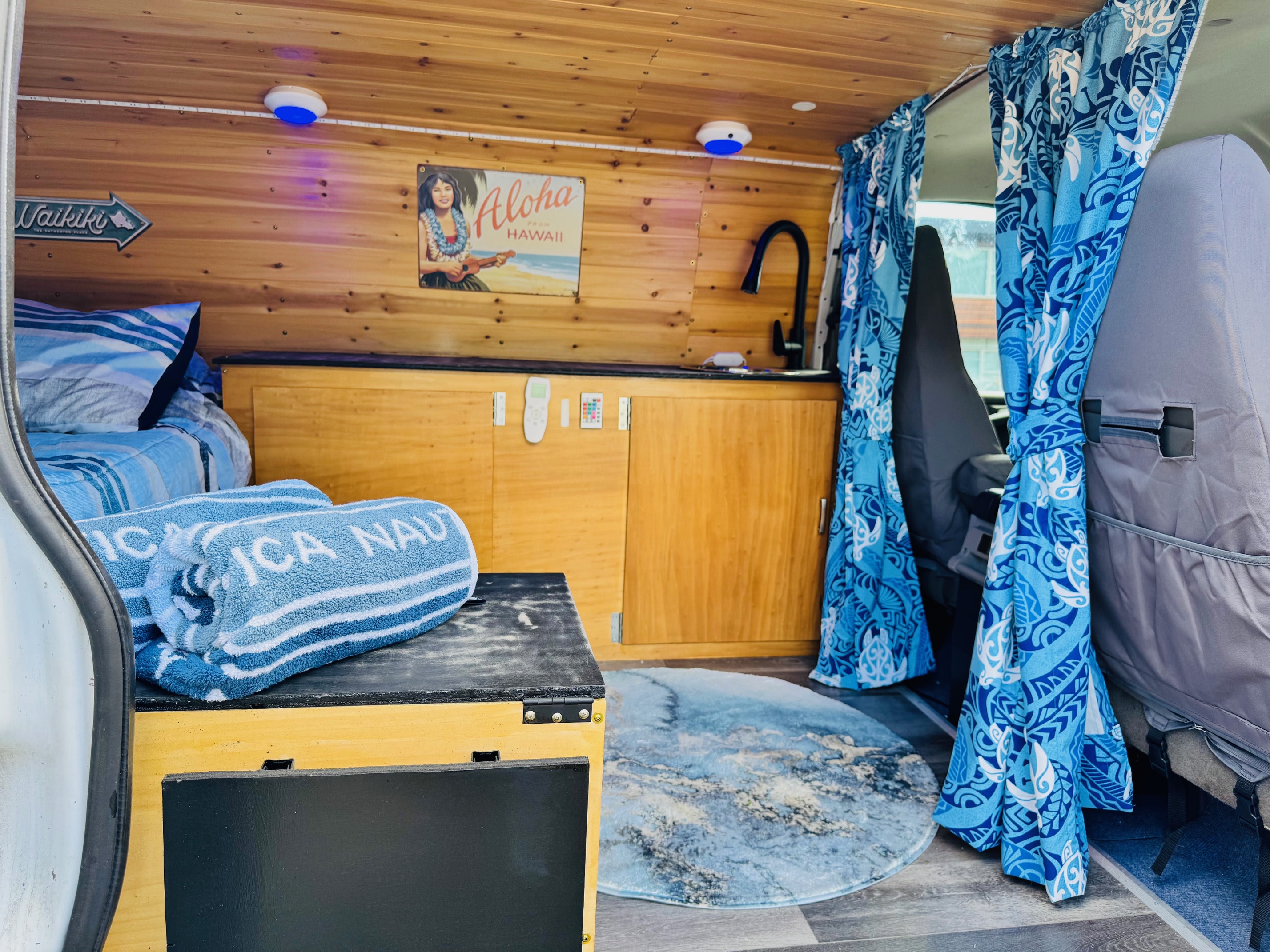 Cozy rv rental interior with Hawaiian-themed decor, including wood paneling, a kitchenette, bed, and vibrant blue accents.. Chevrolet Open Road 2004