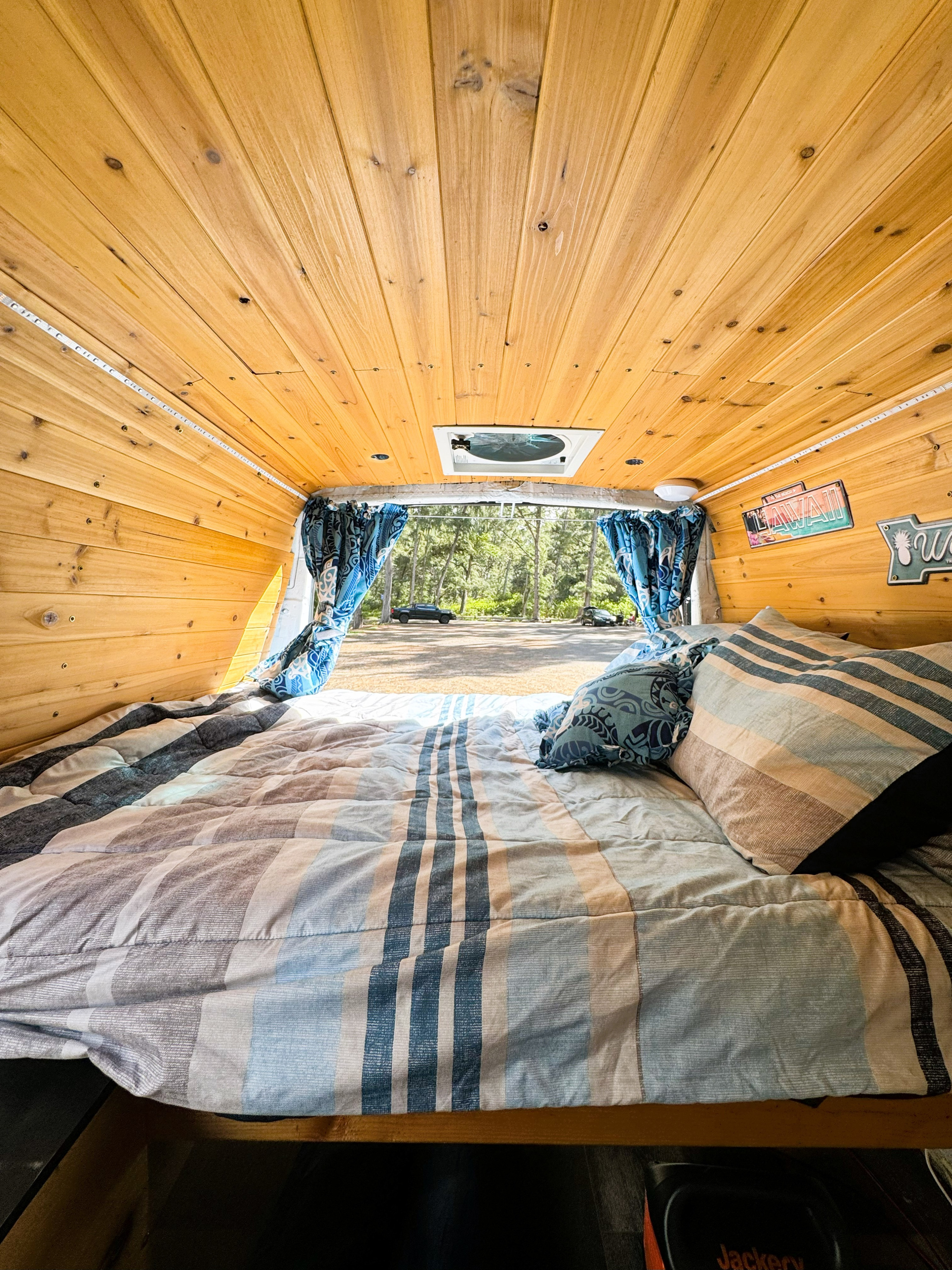 Inside a comfy rv rental camper, this wood-paneled interior features a striped bed looking out to trees and a parking lot.. Chevrolet Open Road 2004