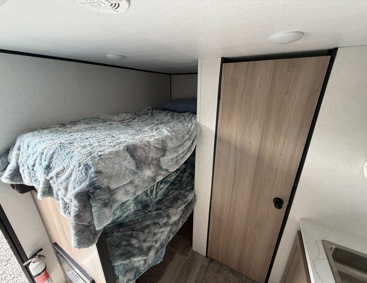 Cozy bunk beds & wooden door inside an RV rental. This compact interior offers comfortable sleeping for your adventure.. Keystone RV Coleman Legacy 2026