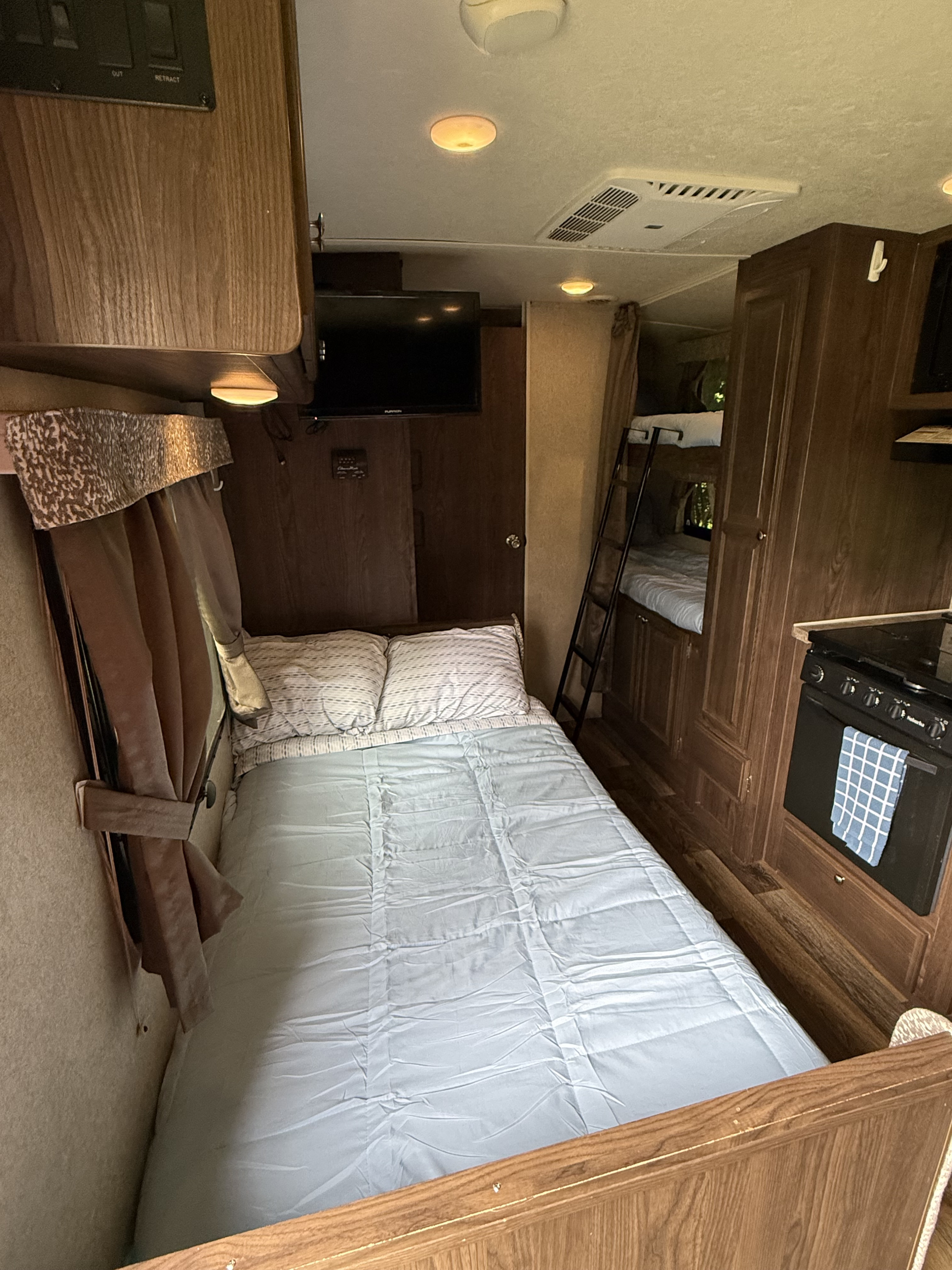 An rv rental's interior features a neatly made bed, bunk beds, a kitchen with an oven, and a TV, providing comfort.. Forest River Rockwood Mini Lite 2016