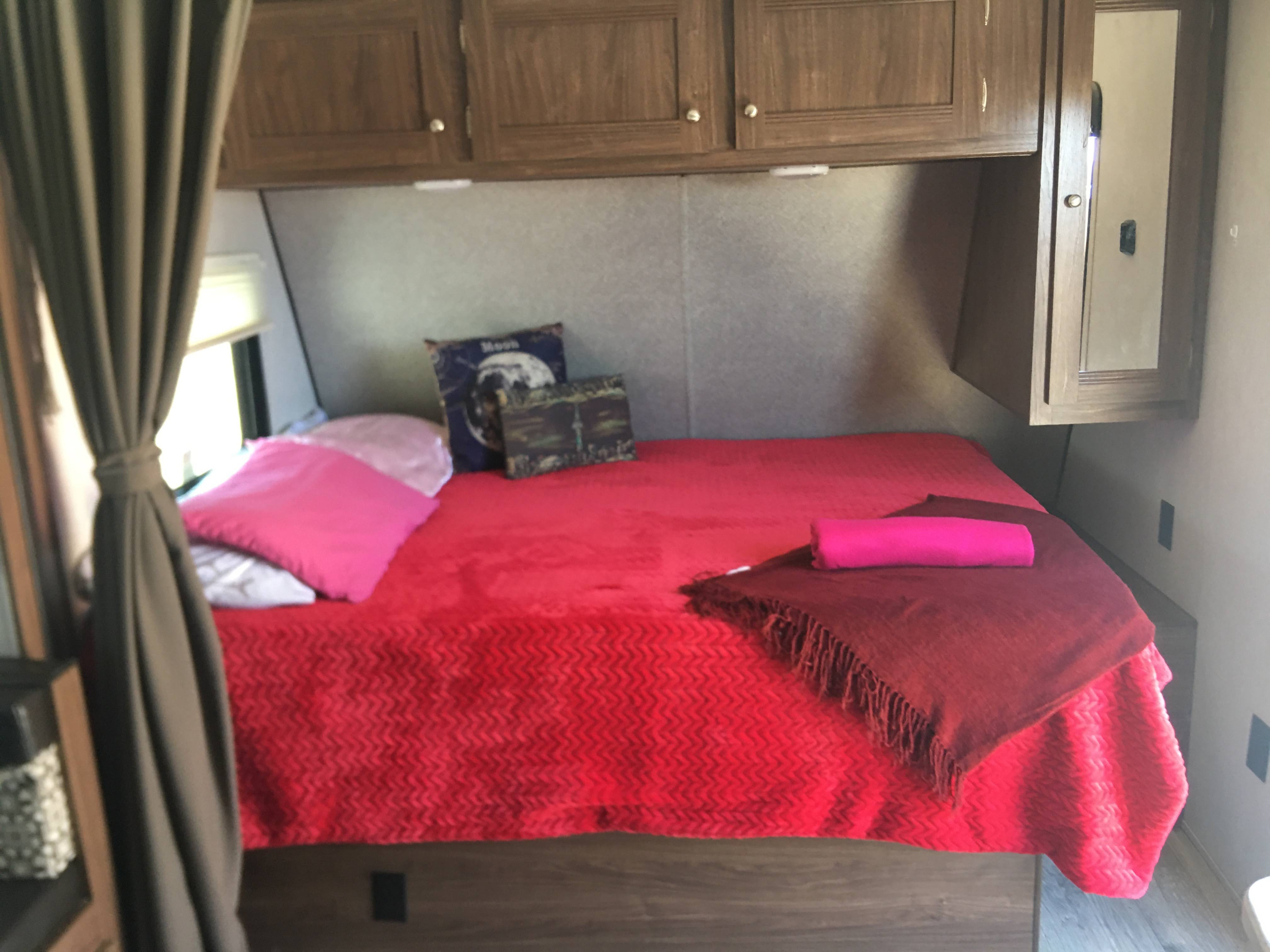 RV rental: A cozy bedroom with red and pink bedding, overhead wooden cabinets, and a curtain by the window.. Heartland Prowler 2019