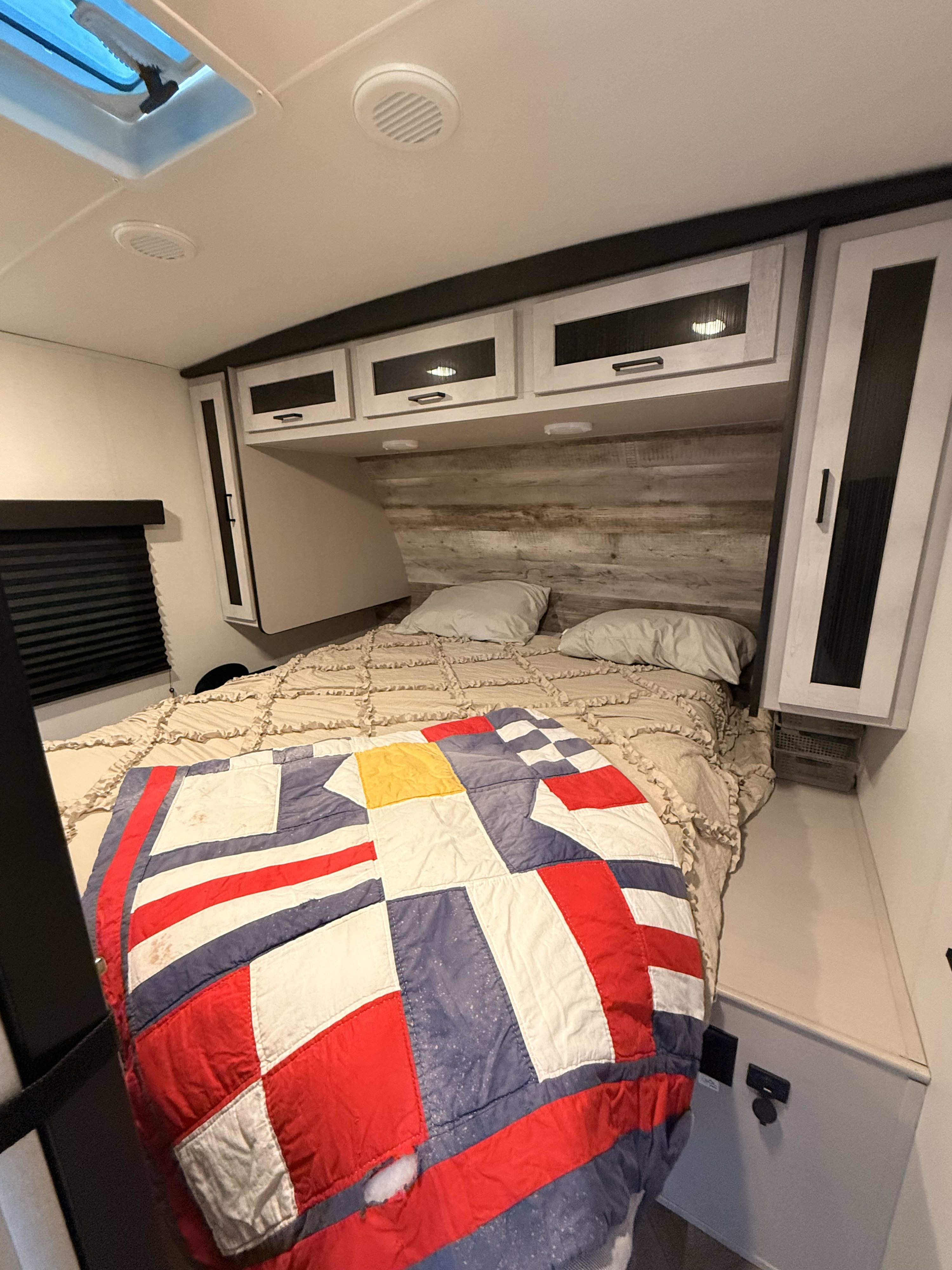 RV rental bedroom featuring a bed with a colorful quilt, overhead cabinets, and a ceiling skylight, offering comfort and storage.. Heartland RVs Mallard 2024