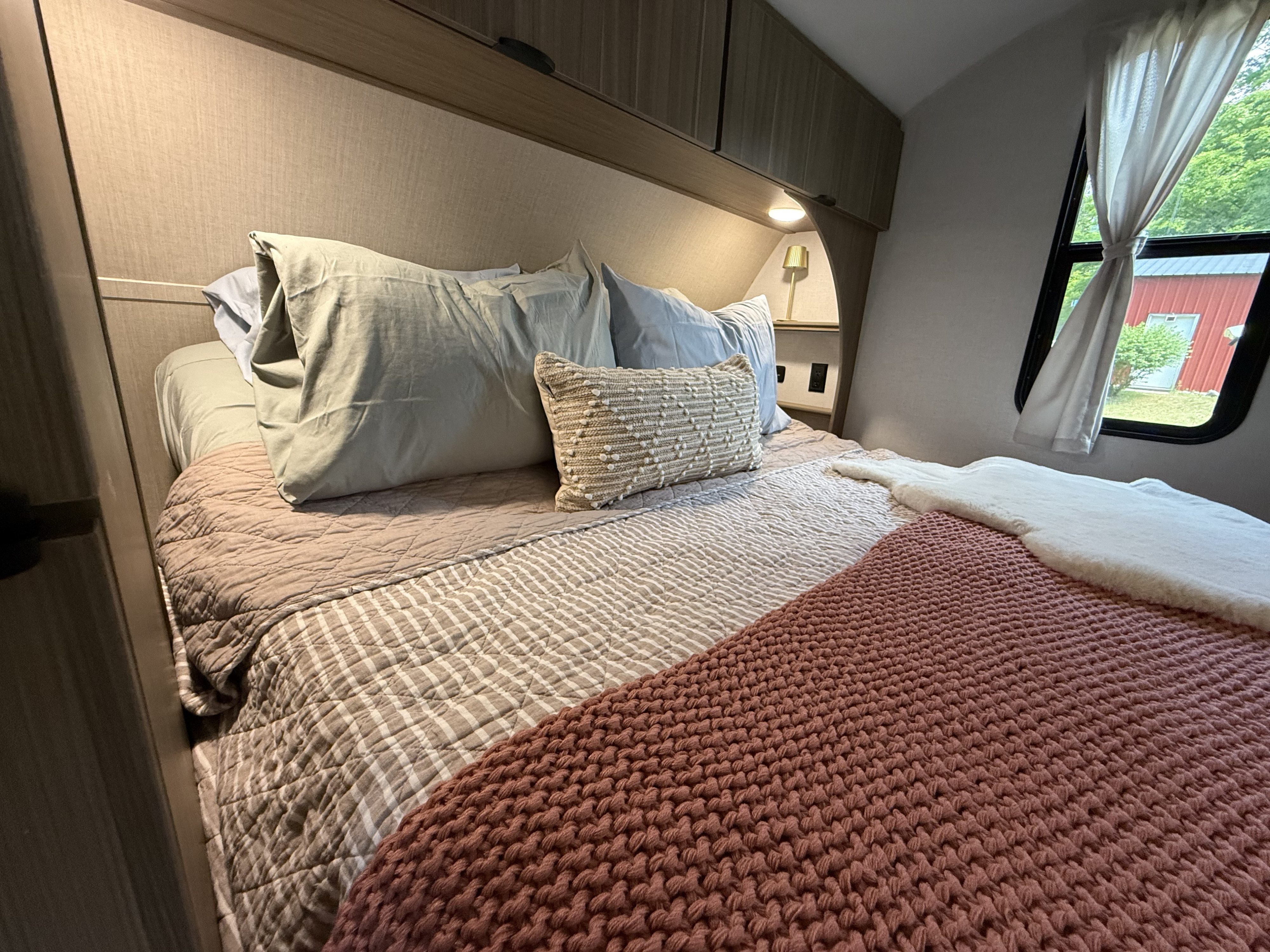 Cozy RV rental bedroom with comfortable bedding, pillows, and a window view. Perfect for travel!. Forest River Wildwood X-Lite 2026