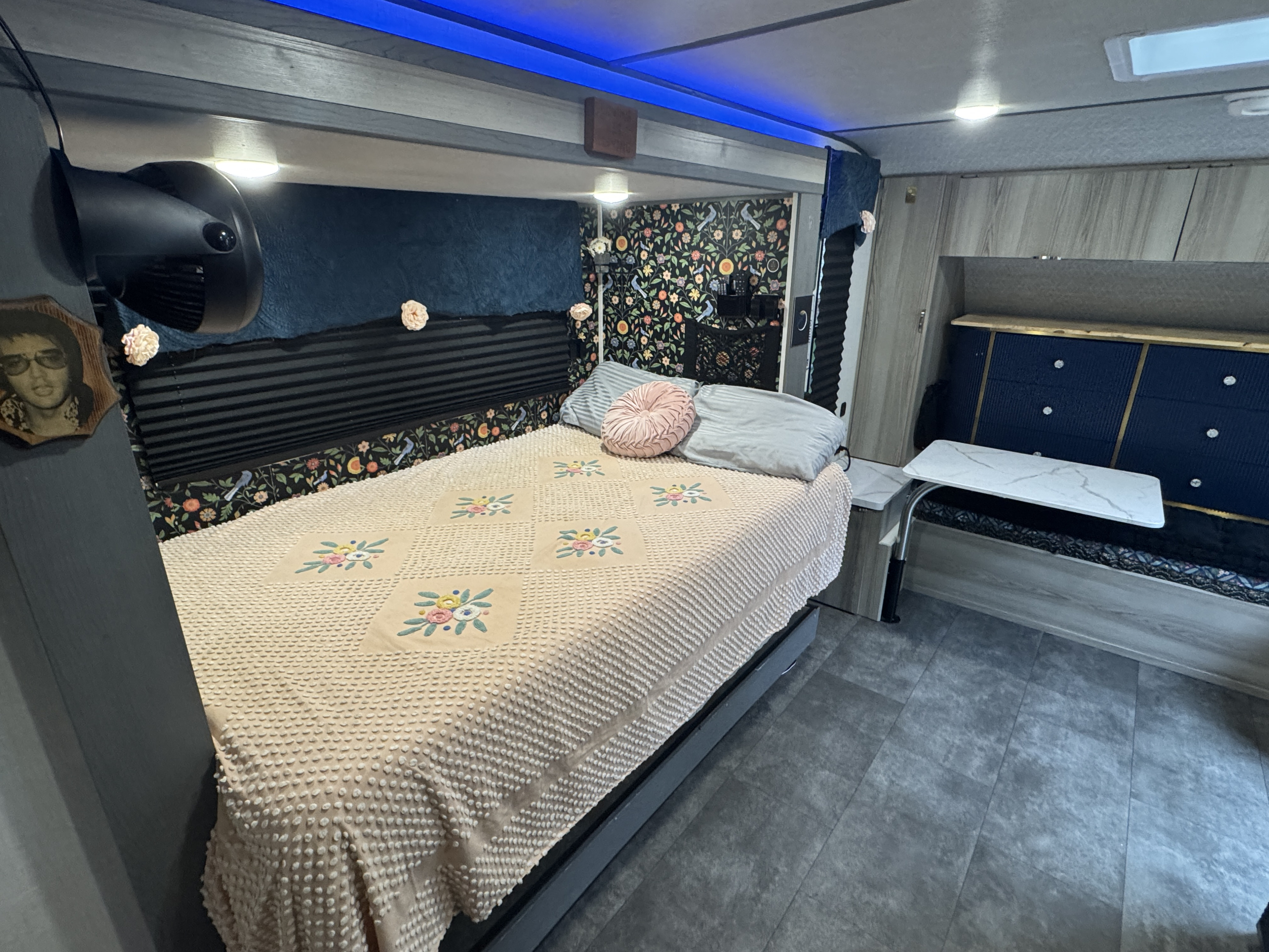 Cozy RV rental bedroom features a floral-decorated bed with a textured comforter, blue LED lights, and a compact dinette.. Forest River Salem FSX 2025