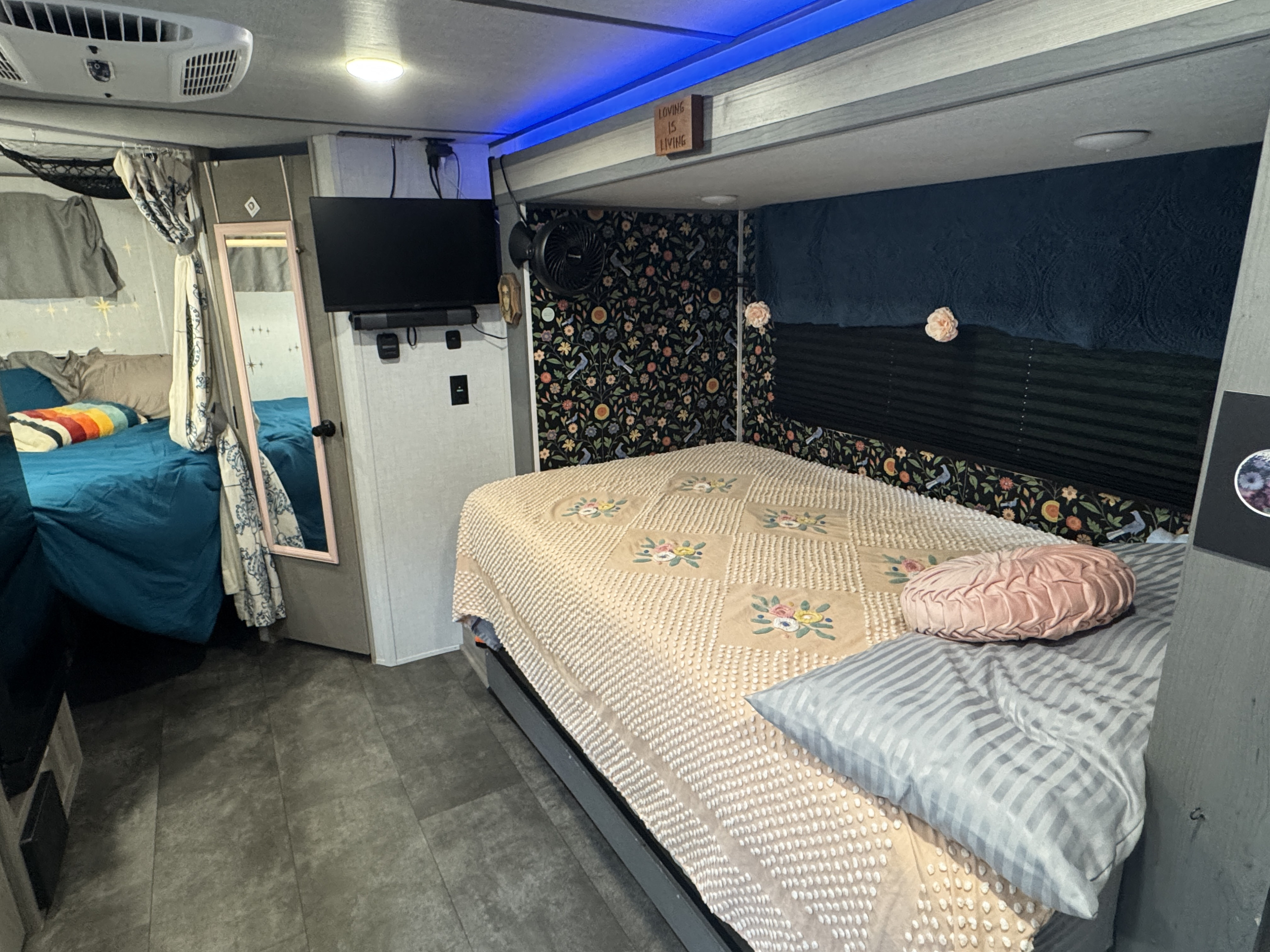 Cozy RV rental bedroom showcasing a large bed, TV, mirror, and bunk. Features unique floral wallpaper, blue accent lights, and an AC unit.. Forest River Salem FSX 2025