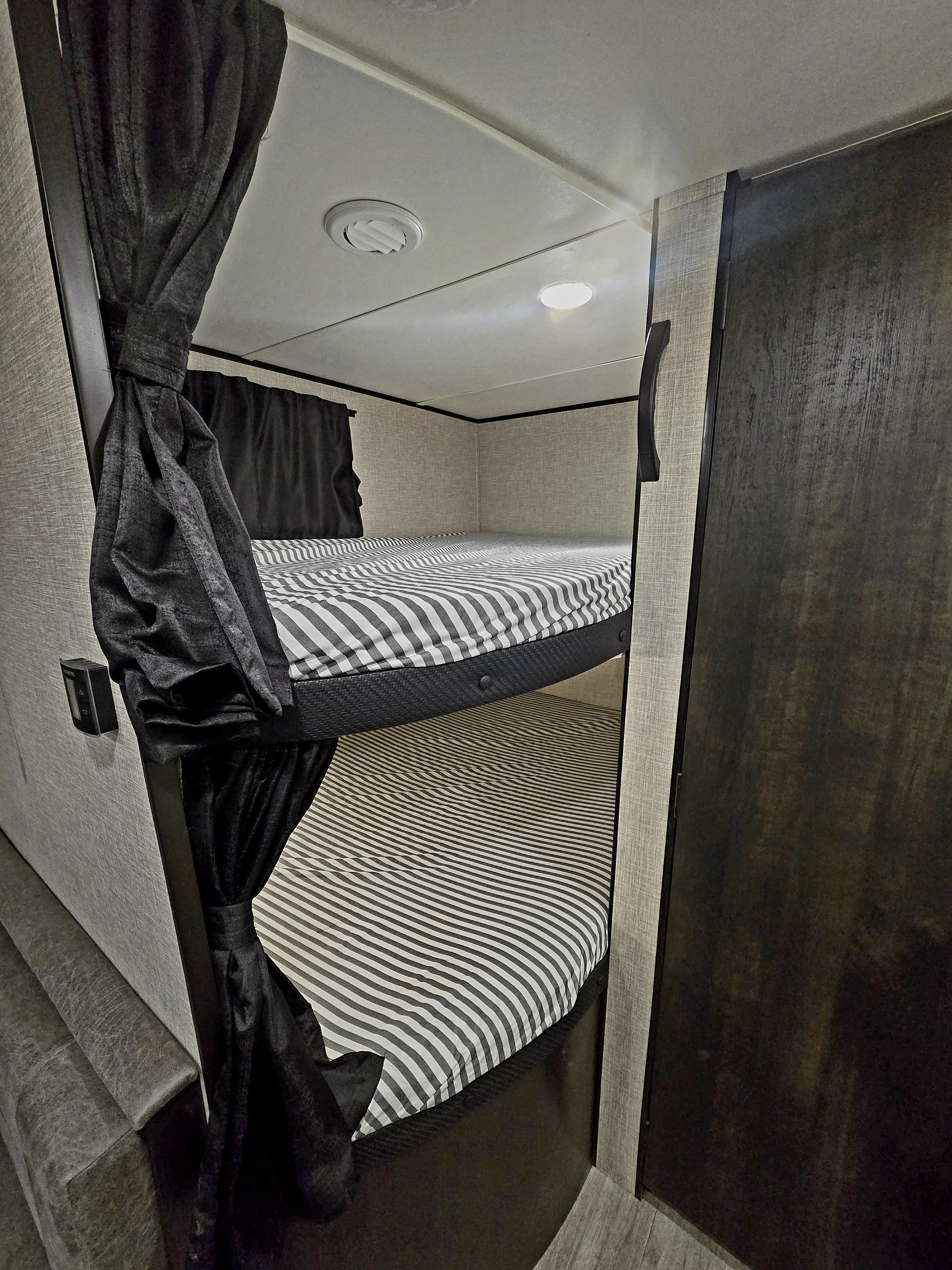 Cozy rv rental interior featuring bunk beds with striped bedding & dark privacy curtains.. Jayco Jay Flight 2023