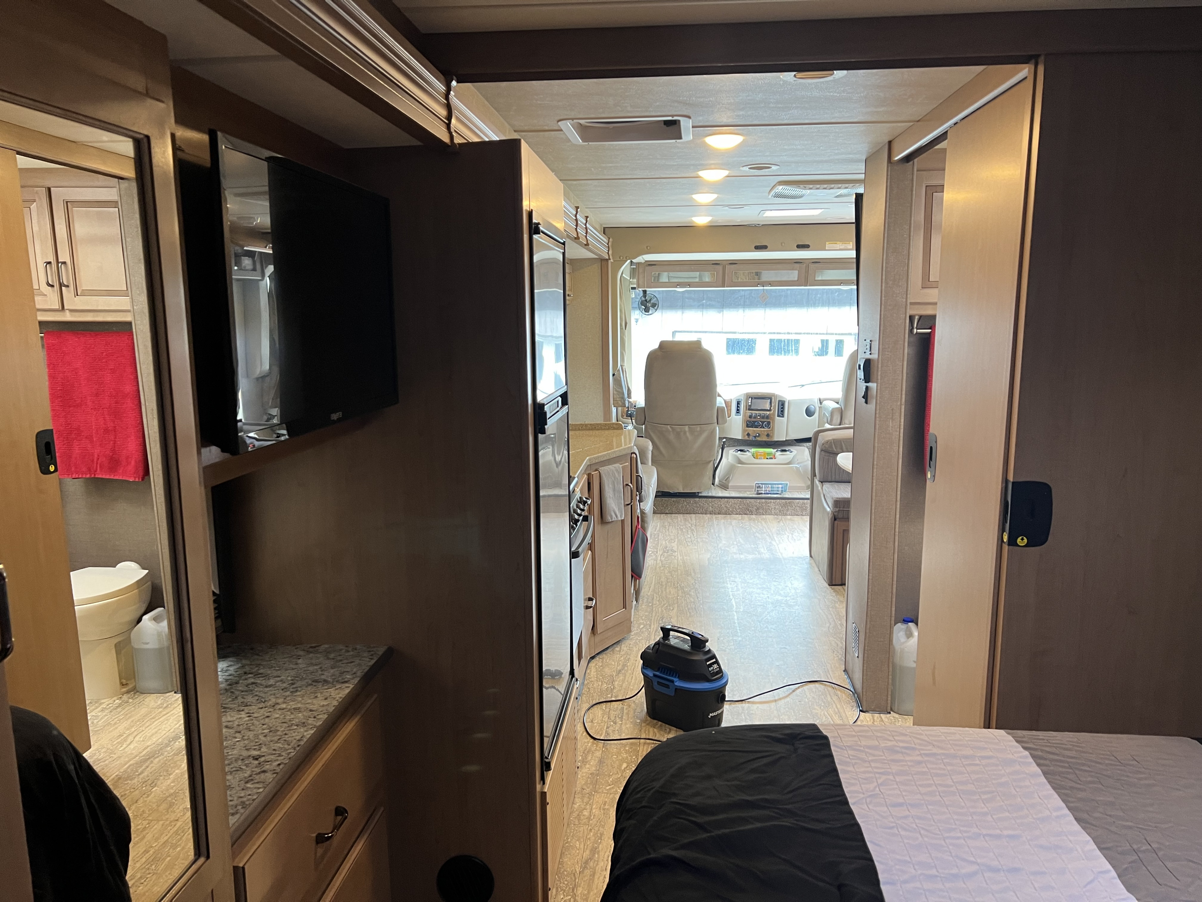 Inside an RV rental: view from the bedroom to the cockpit, passing a kitchen & bathroom. A wet vac is on the floor.. Thor Hurricane 2019