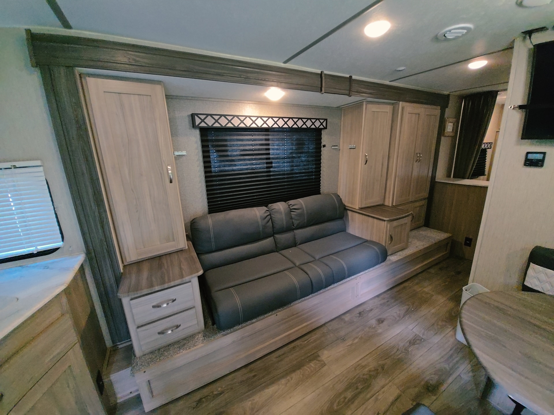 Cozy rv rental living space featuring a gray sofa bed, light wood cabinetry, window blinds, and modern decor.. Coachmen Freedom Express 2021