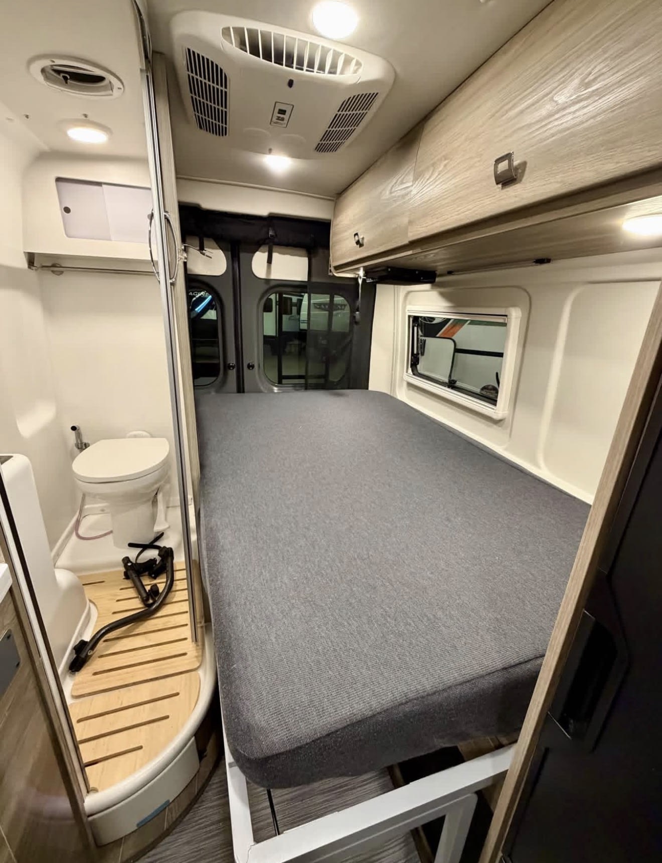 This cozy rv rental interior features a comfortable bed, compact bathroom with toilet, and overhead storage for your road trip comfort.. Winnebago Travato 2023