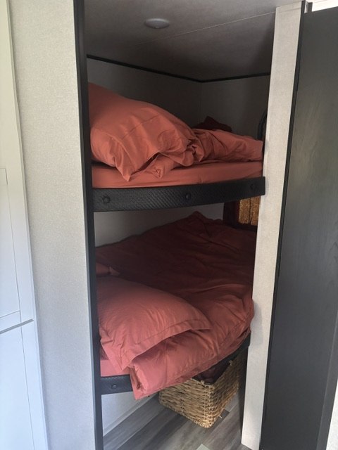 Cozy bunk beds with reddish-orange bedding in an RV rental, offering a compact sleeping area with an under-bunk storage basket.. Jayco Jay Flight SLX 2026
