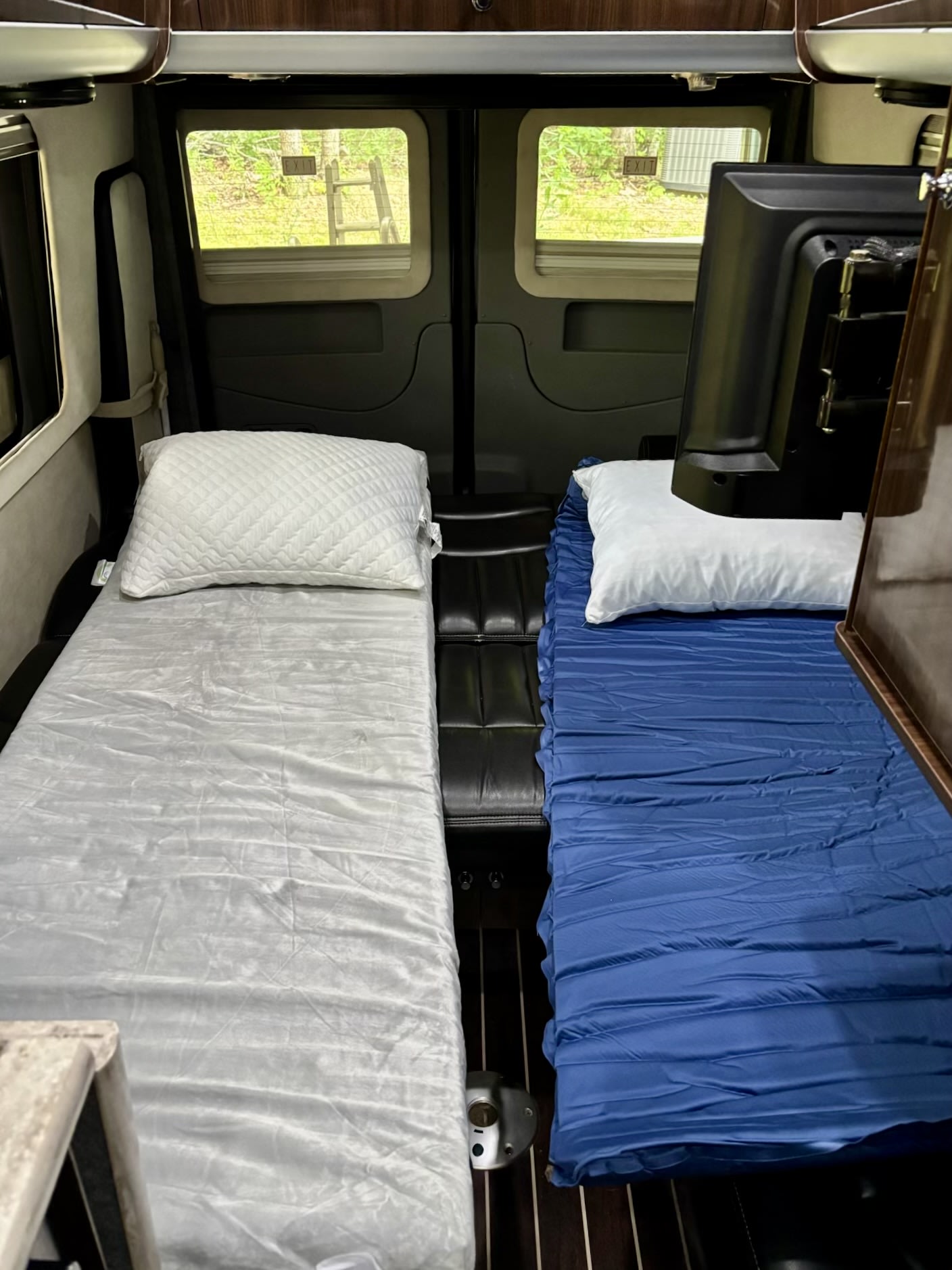 Cozy rv rental interior showing two narrow beds with pillows and bedding, a TV, and rear windows with an 'EXIT' sign.. Airstream Interstate 2016