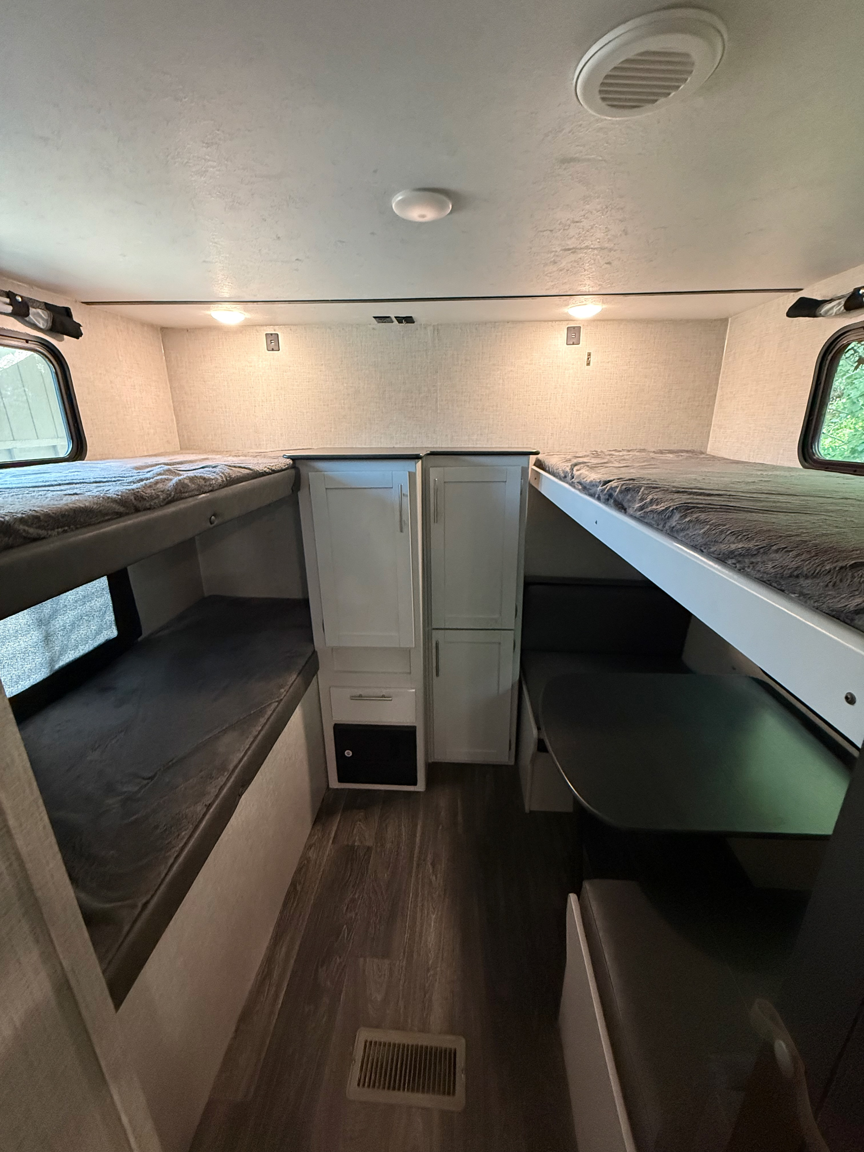 Inside an **rv rental**: dual bunk beds frame a central cabinet, with a dinette on the right. Brightly lit, wood-look floor.. Keystone RV Bullet Ultra Lite 2021